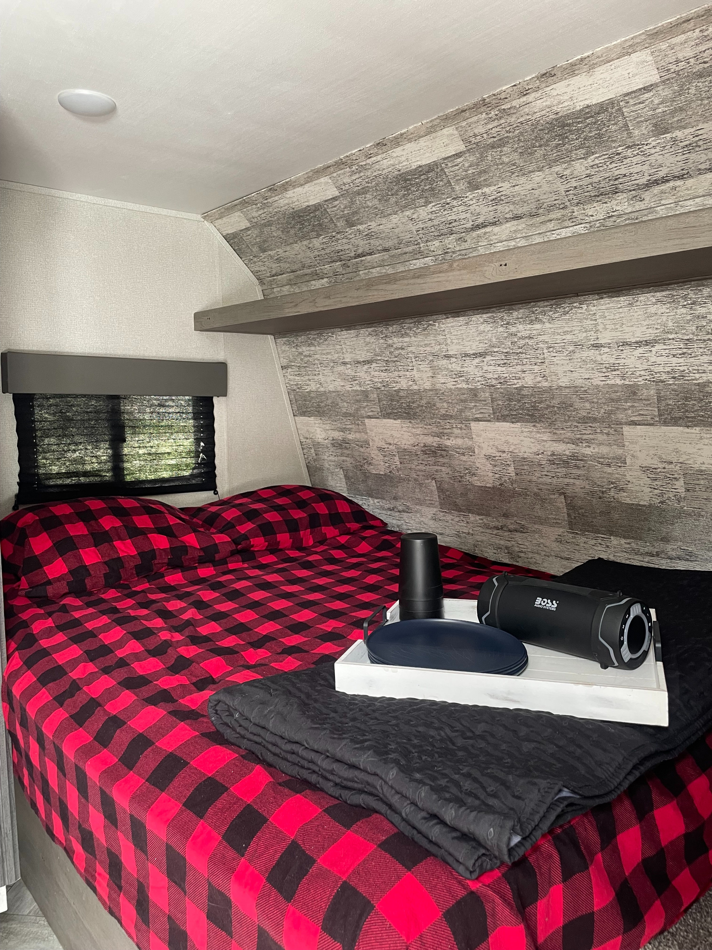 Inside an RV rental: a cozy bedroom with red plaid bedding, a wood accent wall, and a window.. Keystone RV Springdale 2021