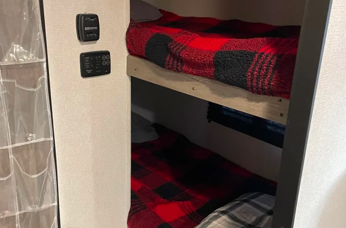 Inside an RV rental: cozy bunk beds with red plaid blankets & essential controls for a comfortable trip.. Keystone RV Springdale 2021