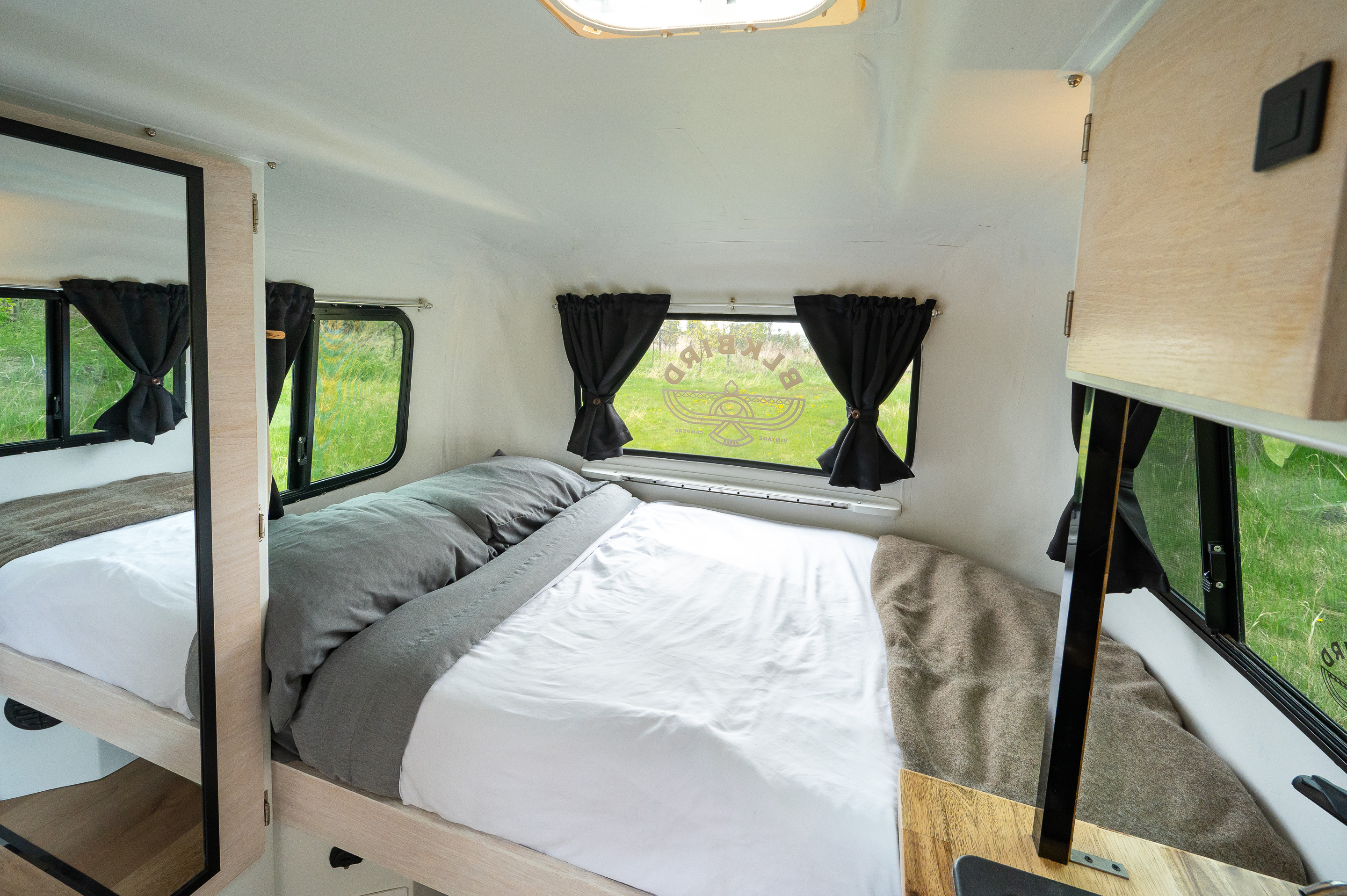 Cozy RV rental interior with a comfortable bed, windows offering nature views, and a full-length mirror.. boler boler 1300 1974