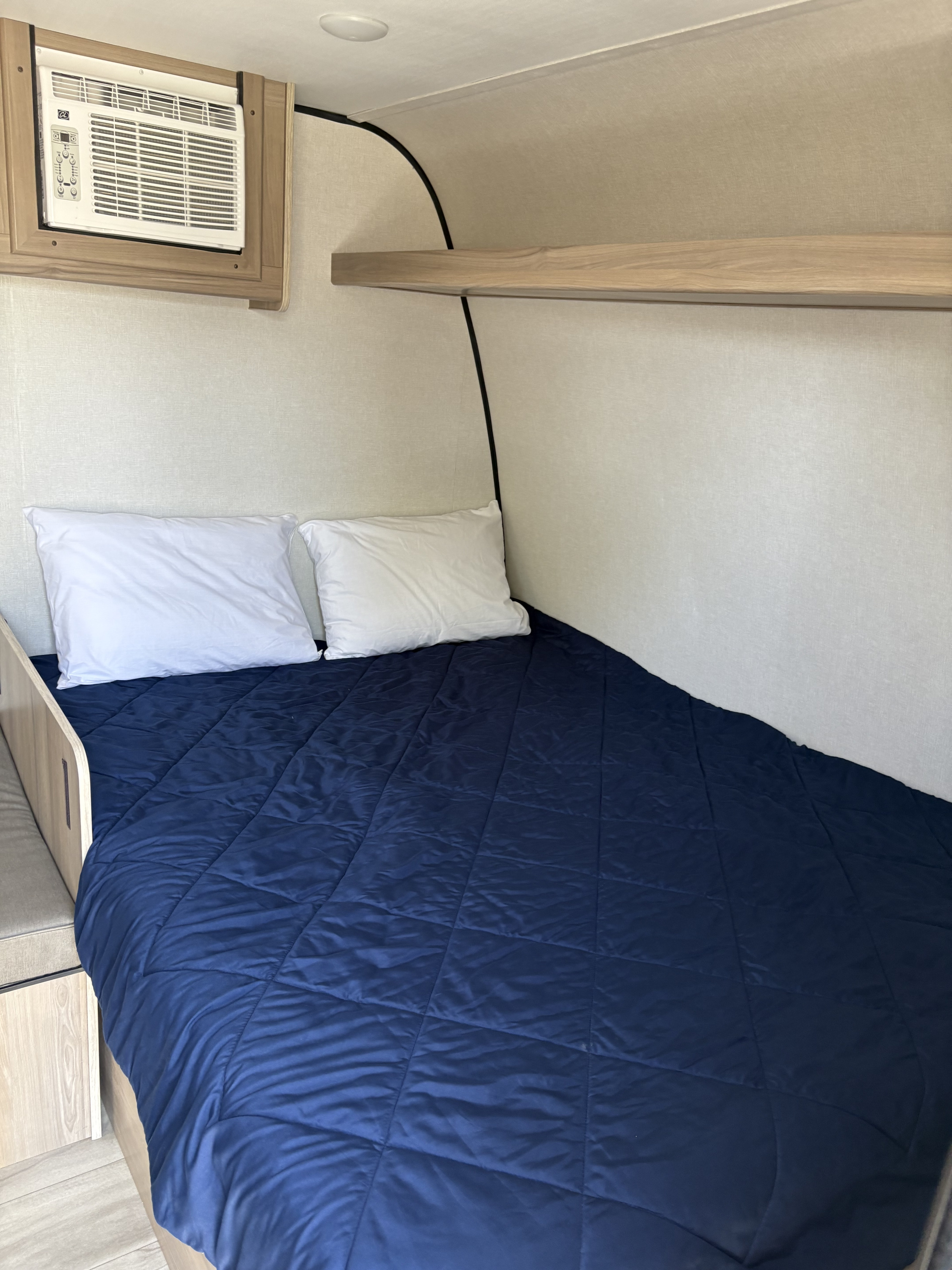 Cozy RV rental bedroom: dark blue comforter, white pillows, AC, and shelving. Ideal for comfortable travel.. Coleman 17B 2025