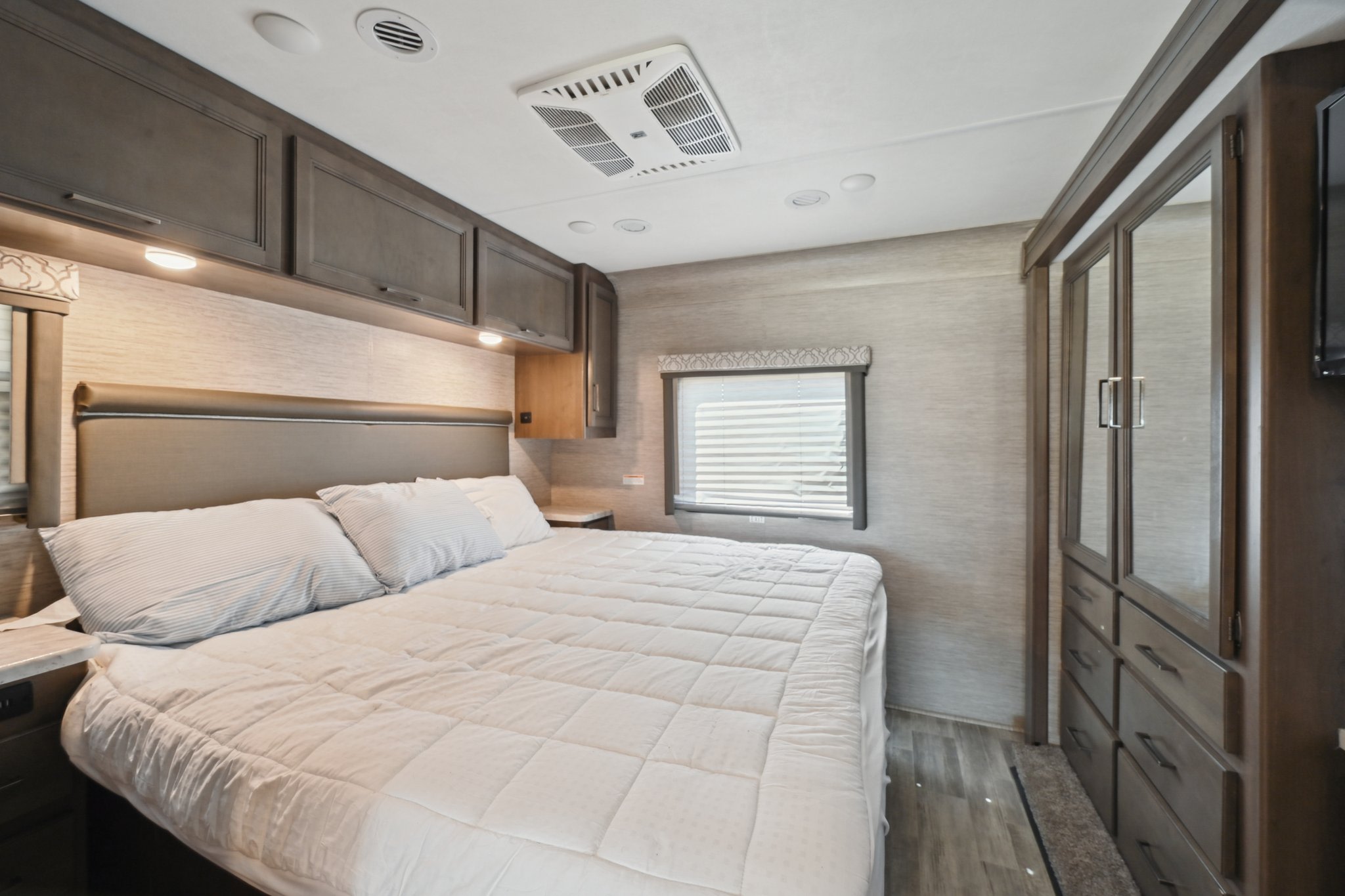 An RV rental bedroom featuring a large bed, overhead cabinets, and built-in mirrored wardrobe, ideal for comfortable travel.. Thor Freedom Traveler 2022