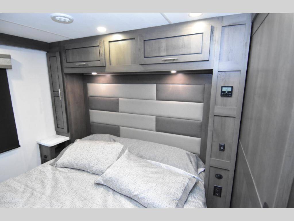 Cozy RV rental bedroom features a plush headboard, ample overhead storage, and bedside controls for convenience.. Georgetown 33B3 2024
