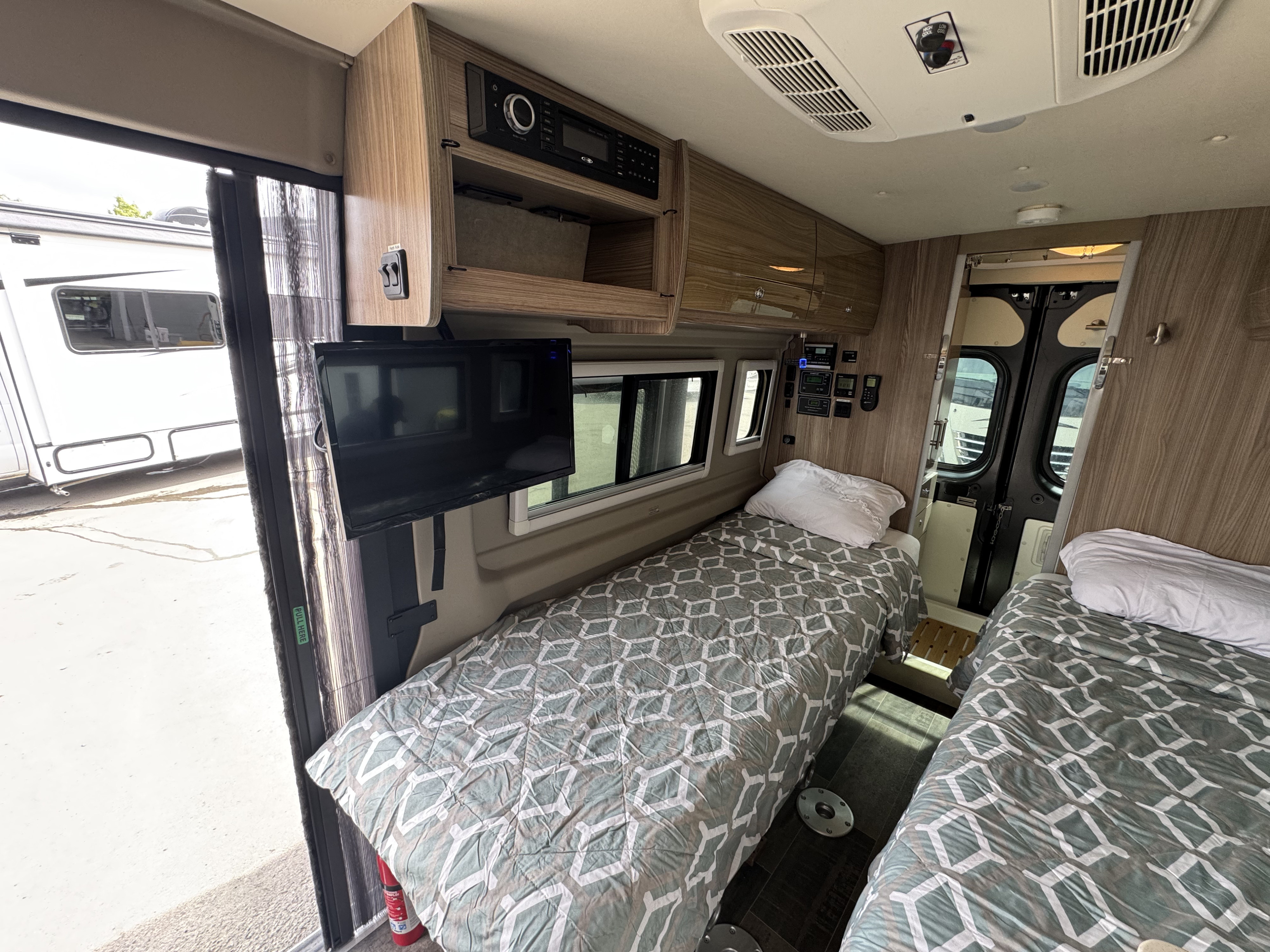 Inside an RV rental: twin beds with patterned comforters, TV, and essential controls for your adventure.. Winnebago Travato 2018
