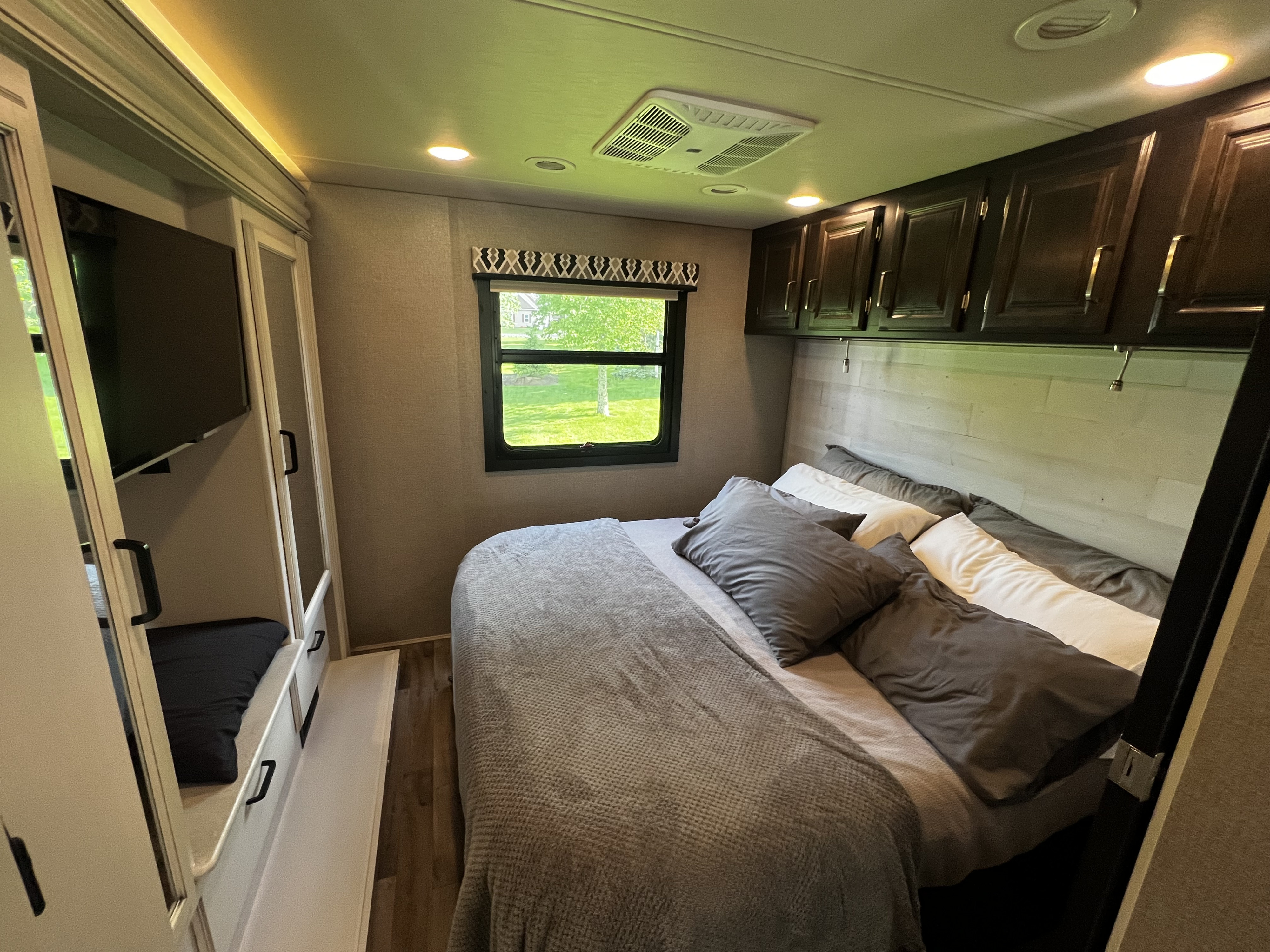 Explore this comfortable RV rental bedroom, featuring a full bed, storage cabinets, a window, and a TV.. Jayco Precept 2020