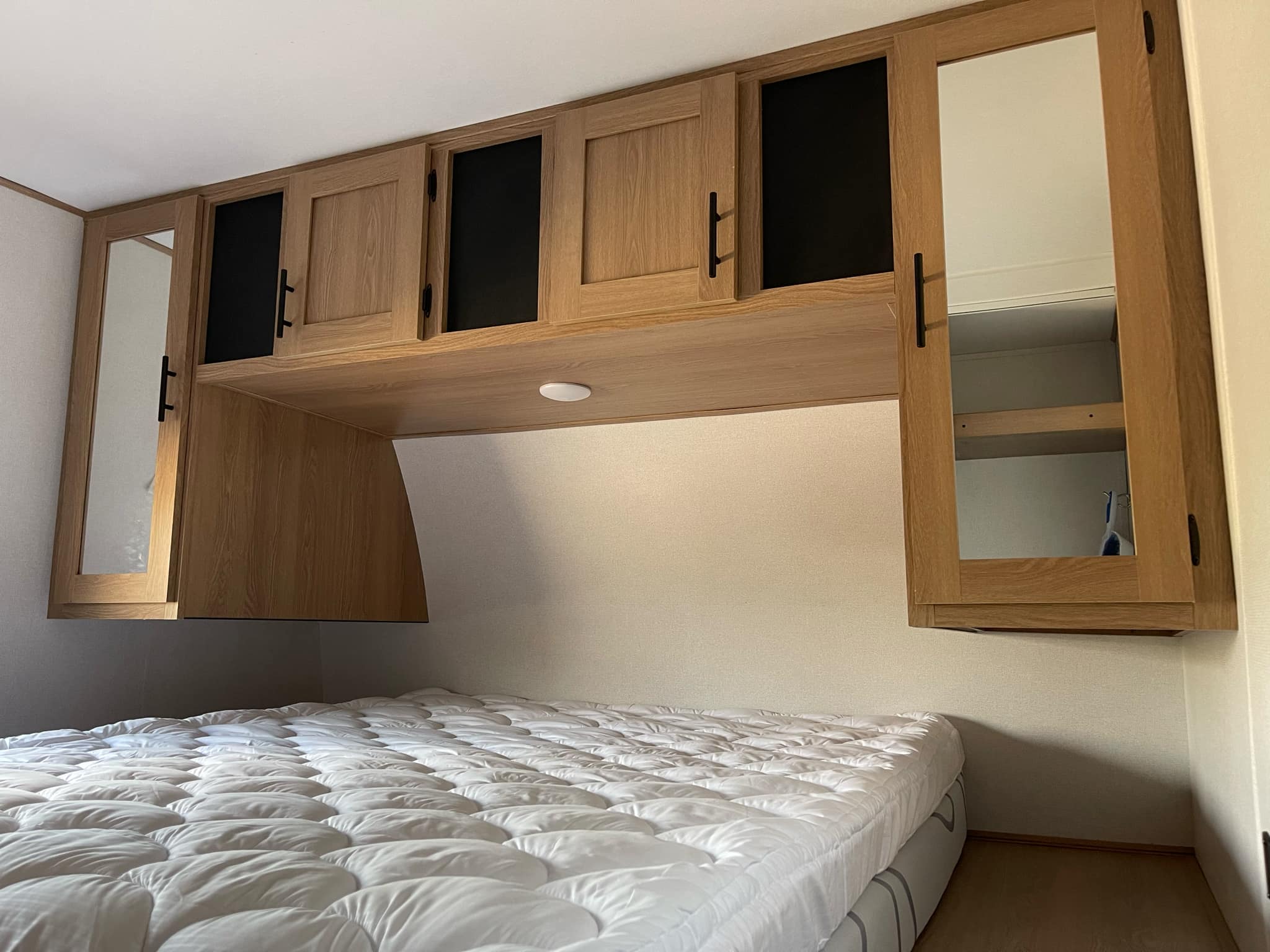 Cozy RV rental bedroom with a comfortable bed and light wood overhead storage cabinets, some featuring mirrored doors.. Avenger Avenger Trailer 2022