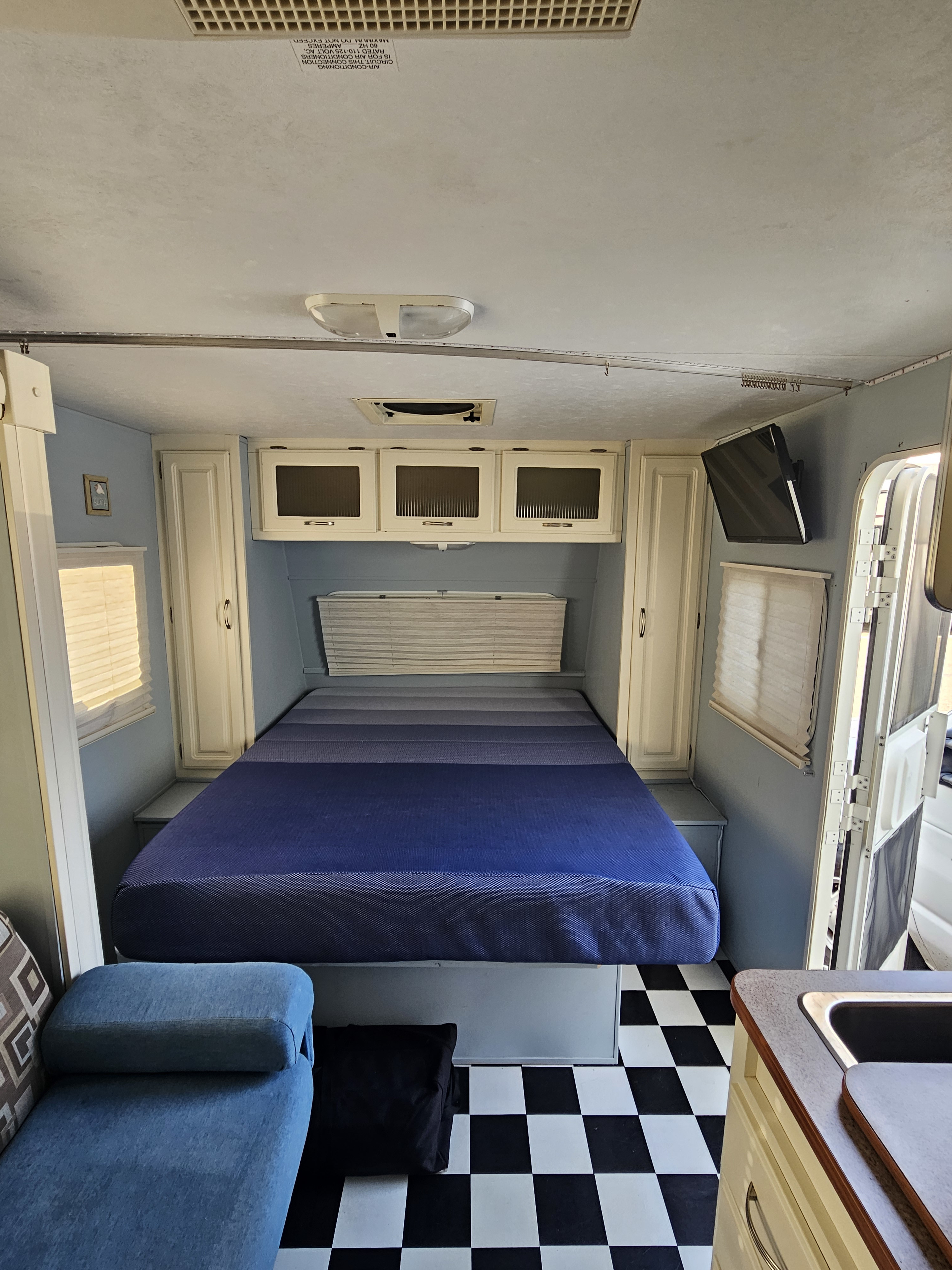 Cozy RV rental interior with a spacious bed, light blue walls, and a classic checkerboard floor, offering compact comfort.. Cruiser RV Fun Finder X 2008