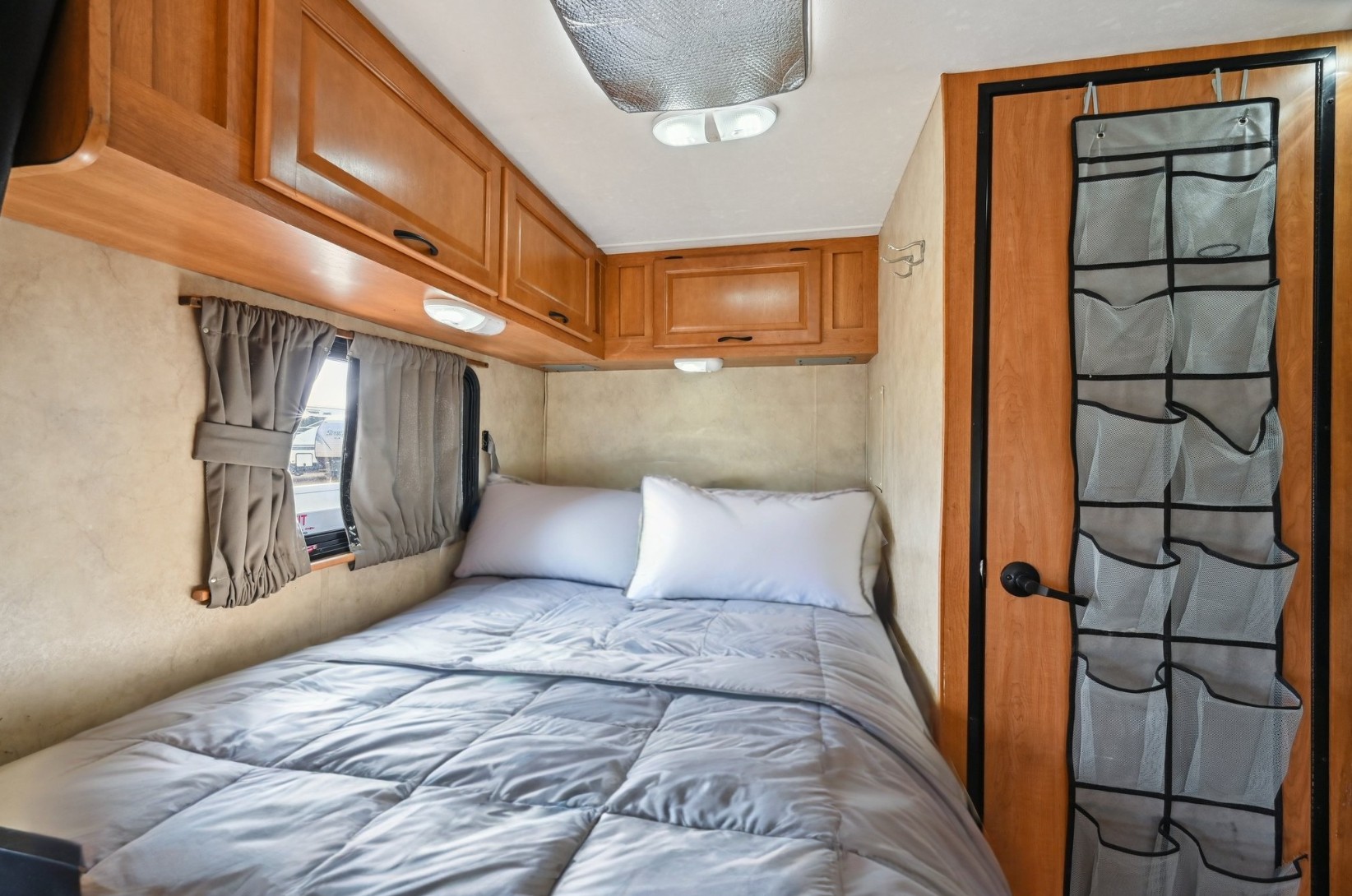 Inside an RV rental: a cozy bedroom with a neatly made bed, wooden cabinets, and an over-door organizer for convenience.. Thor Motor Coach Four Winds Majestic 2013