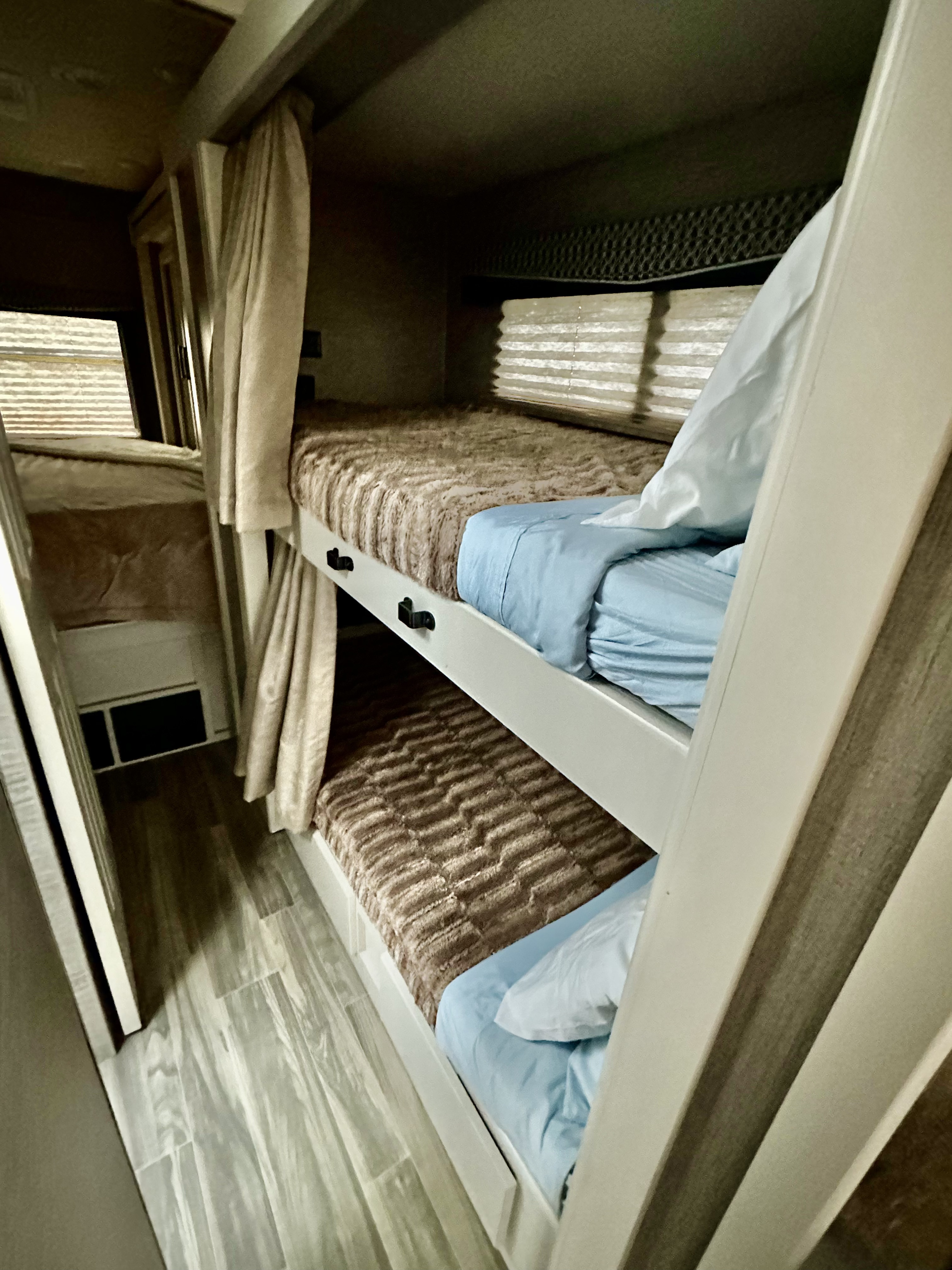 Cozy bunk beds inside an RV rental, featuring soft linens, privacy curtains, and window blinds for comfortable travel.. Thor A.C.E. 2021