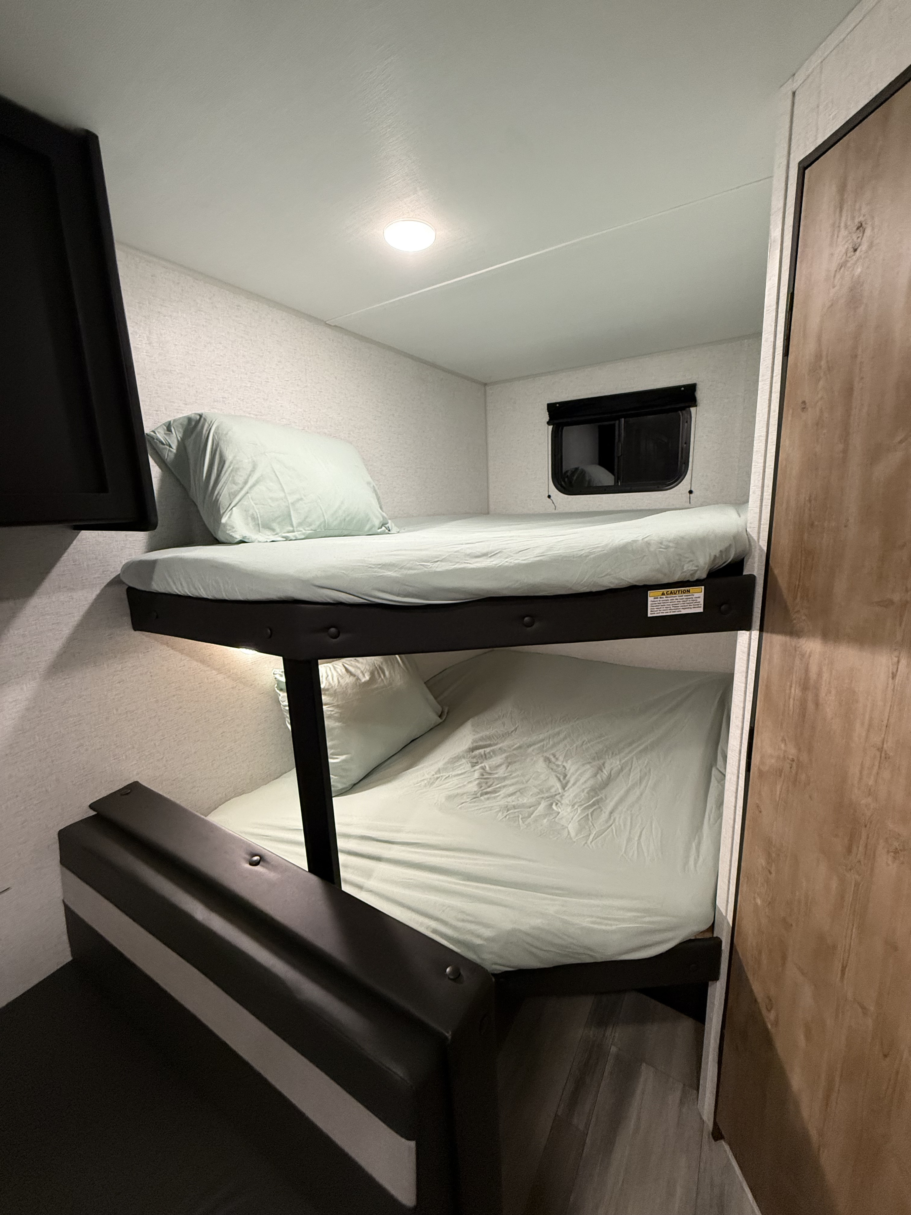 Cozy bunk beds in an RV rental, with light green sheets, a window, and a versatile lower bunk seating.. Keystone RV Springdale 2023