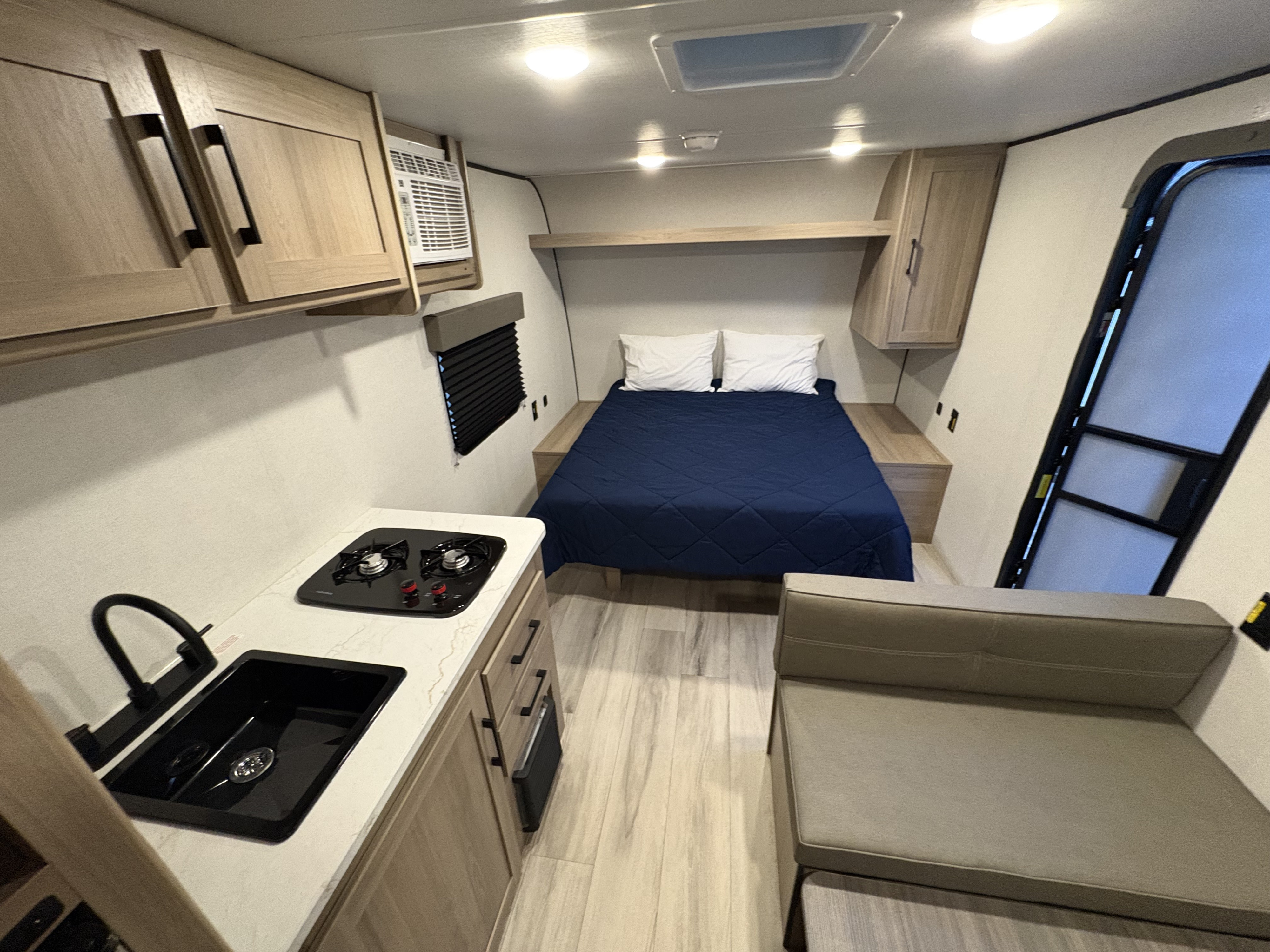 Experience this RV rental's well-designed interior, featuring a cozy bed, kitchen, and sofa seating.. Coleman 17R 2025