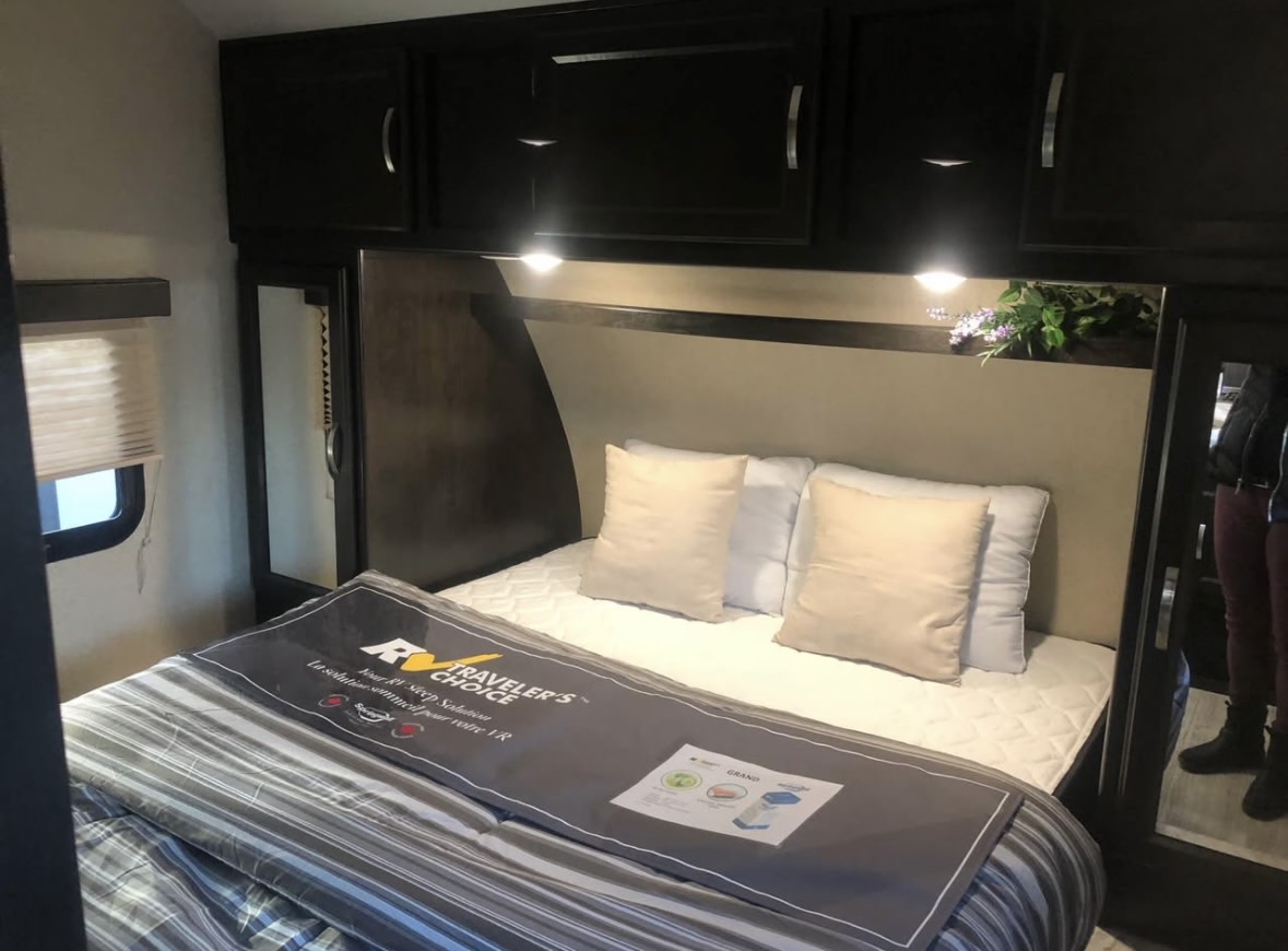 RV rental bedroom interior: comfortable bed with pillows, dark overhead cabinets, a side window, and mirrored closet.. Crossroads RV northern spirit 2019