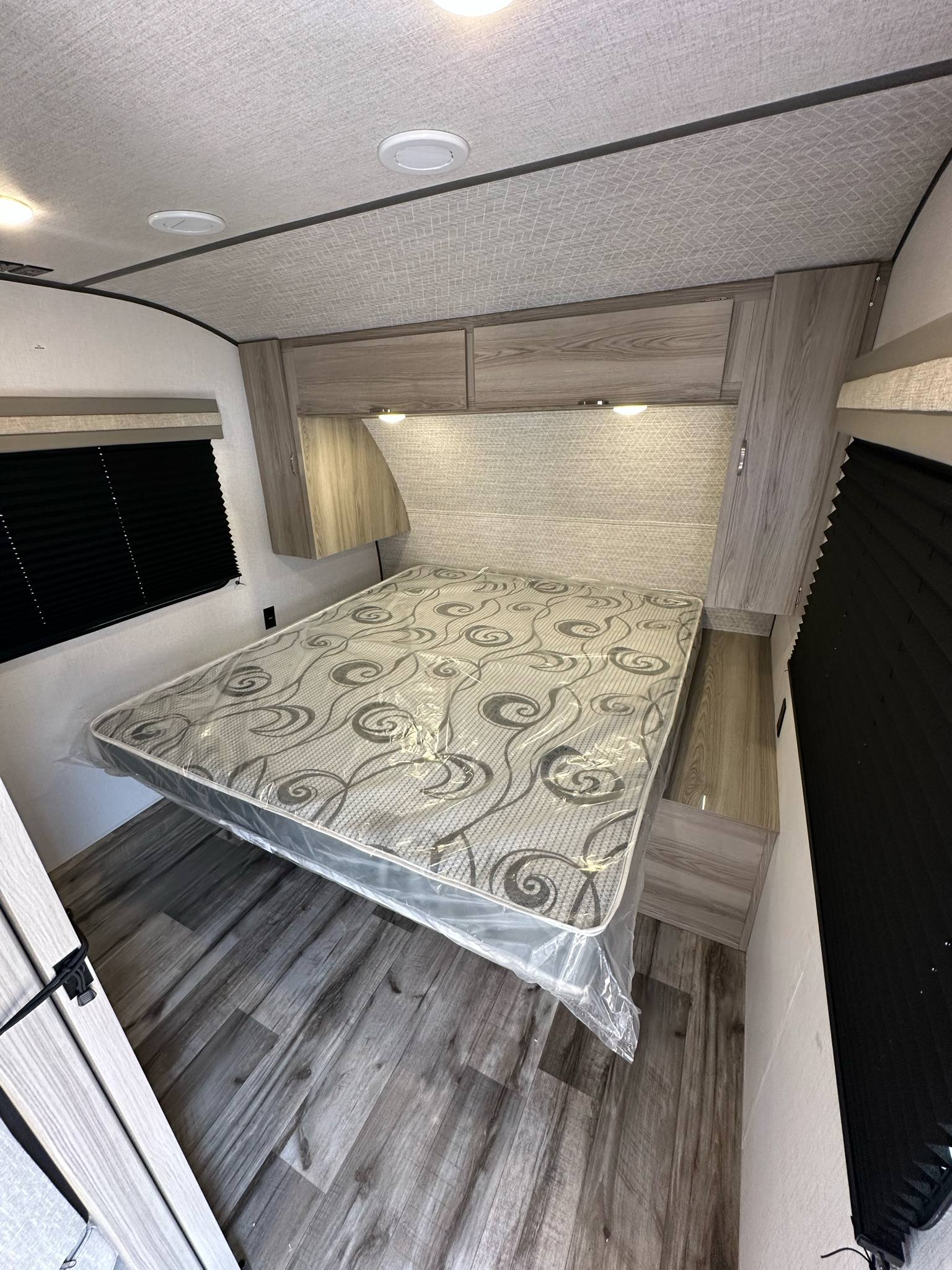 Modern RV rental bedroom with a comfy bed, overhead cabinets, and dark wood-look flooring. Ready for your adventure!. Forest River Salem FSX 266BHLE 2025