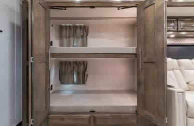 Inside this RV rental, find compact bunk beds with mattresses & curtains, framed by open wooden doors. Cream seating is visible right.. Forest River Georgetown 2022
