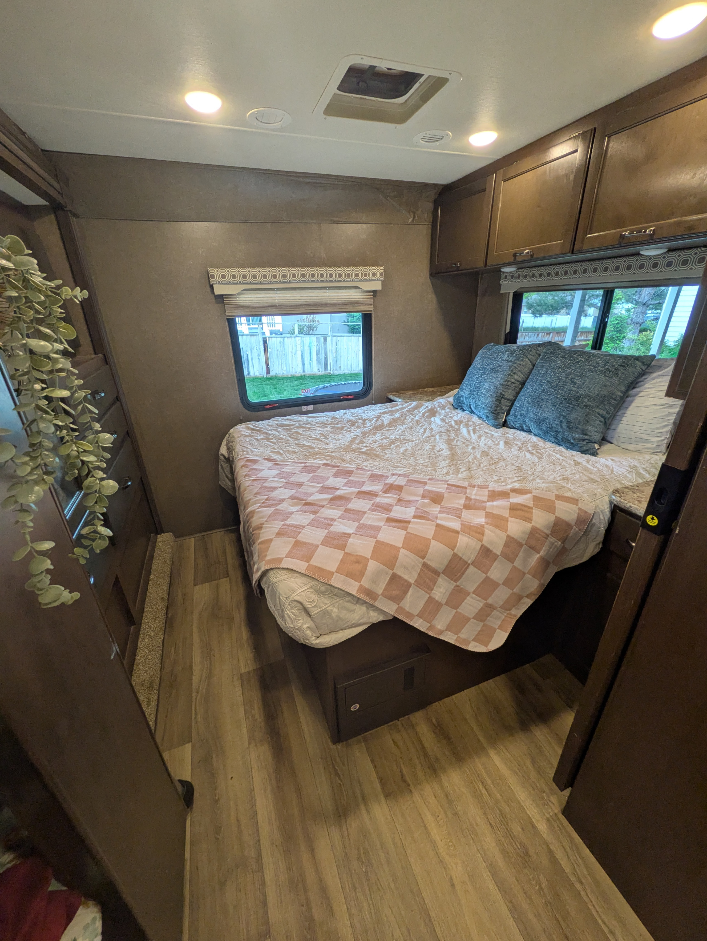 Cozy RV rental bedroom featuring a full-size bed with patterned bedding, overhead cabinets, and a side window.. Thor Four Winds 2020