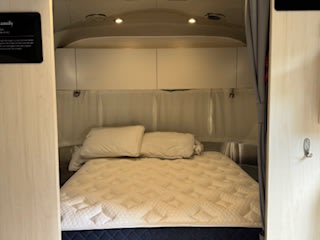 Inside a modern rv rental: a cozy camper bedroom with a comfortable bed, white linens, and overhead cabinets for storage.. Airstream Flying Cloud 2023