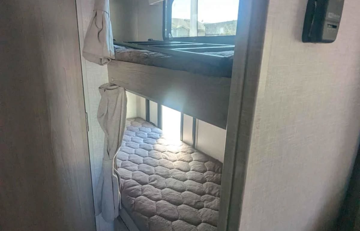 Inside an RV rental: view of comfortable bunk beds with soft mattresses, privacy curtains, and a ladder for the top bunk.. Forest River Rockwood Geo Pro 2021