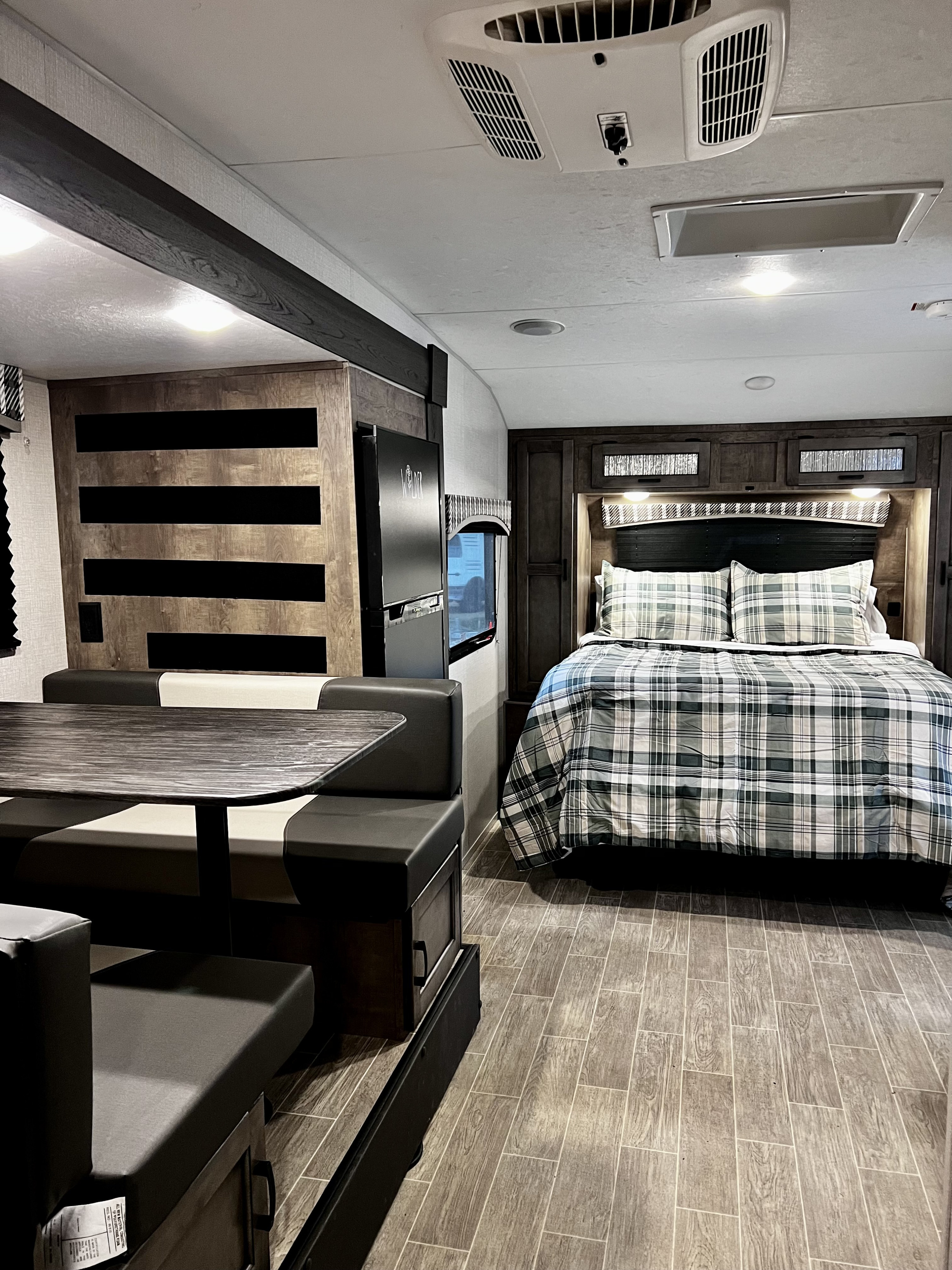 Cozy RV rental interior showing a comfortable bedroom with plaid bedding, a dinette, and modern wood-look flooring.. Venture Sonic 2022