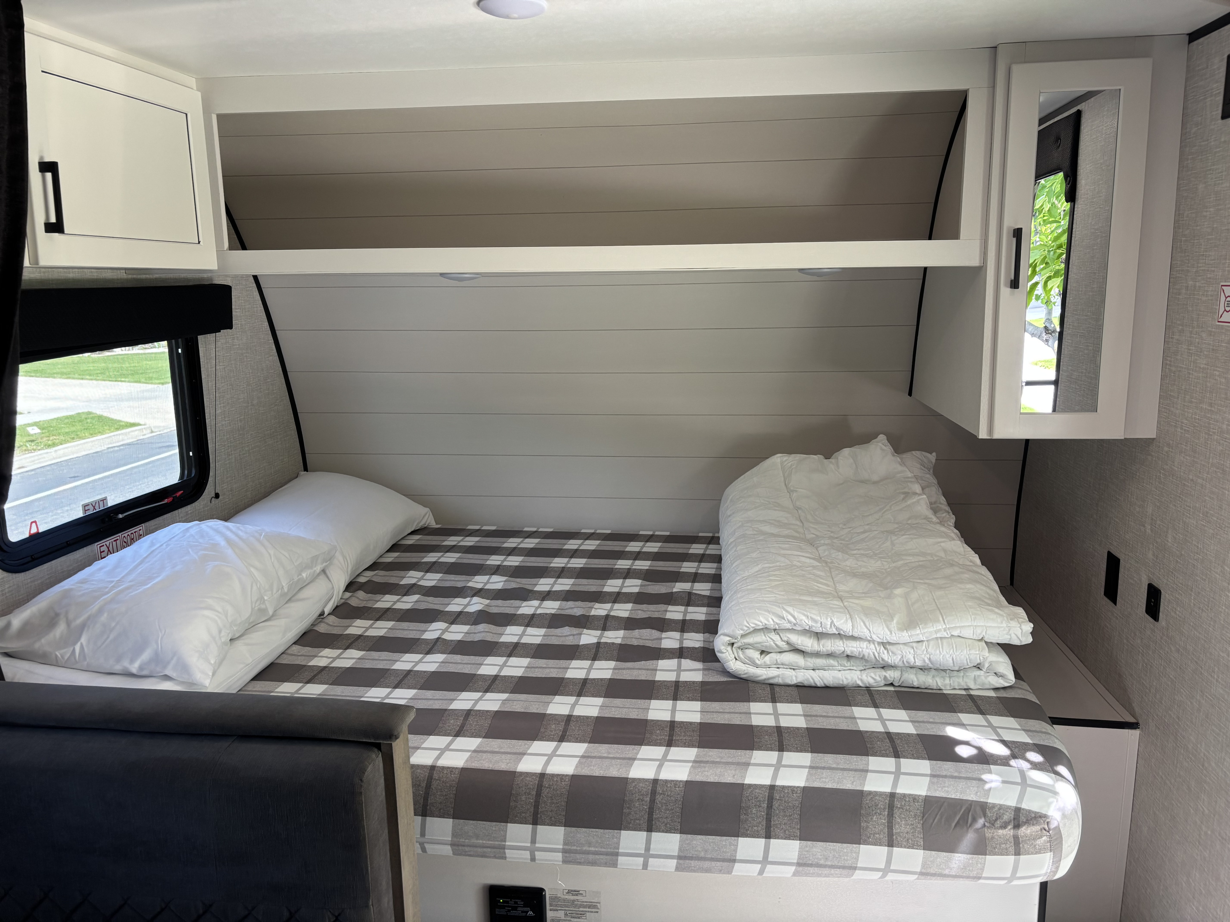 Inside an RV rental: a cozy bedroom with a grey plaid bed, white pillows & comforter, overhead cabinets, and a window view.. Jayco Jay Flight SLX 175BHW 2025