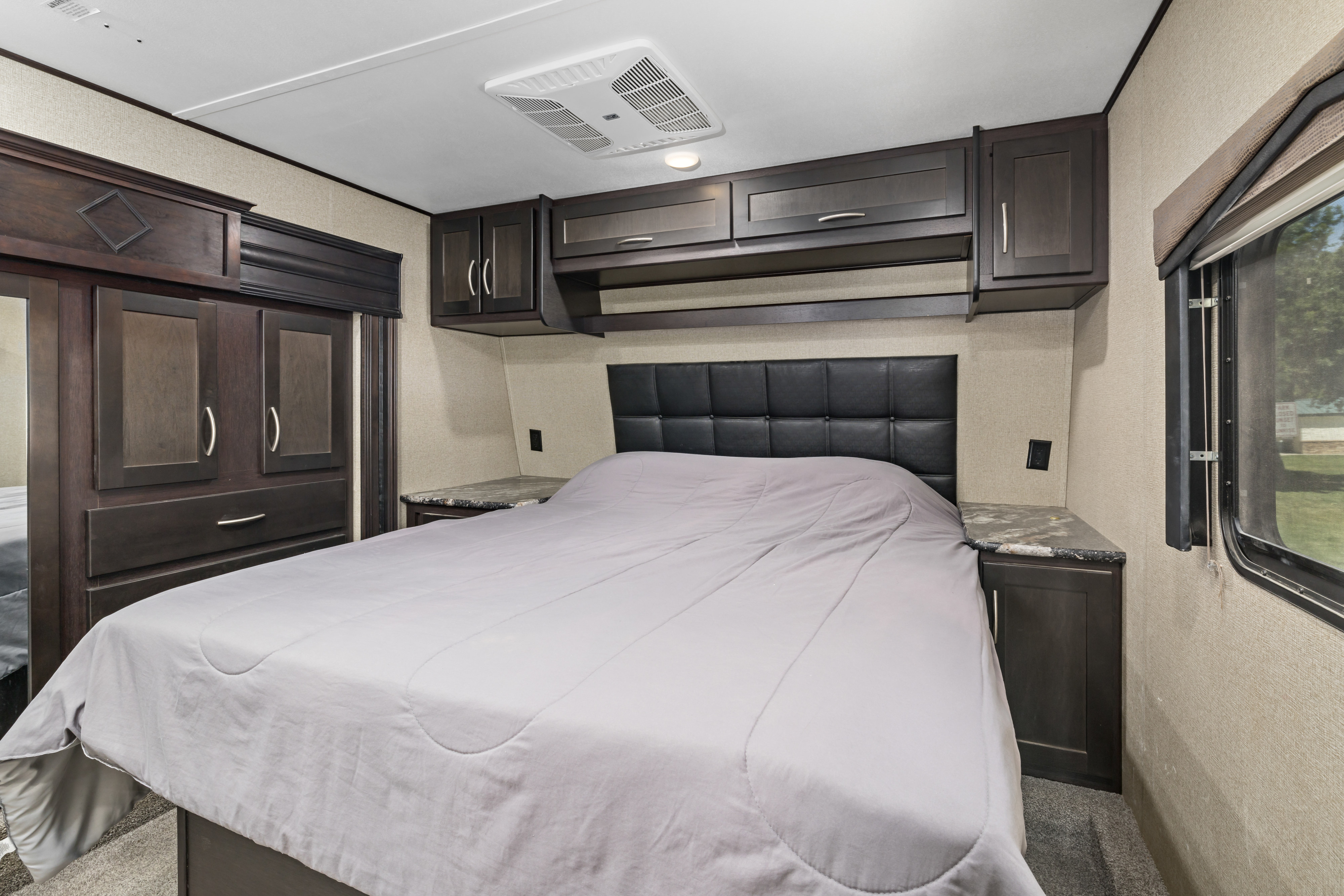 Spacious RV rental bedroom featuring a large bed, dark wood cabinets, and built-in storage.. Keystone RV Carbon Toy Hauler 2018