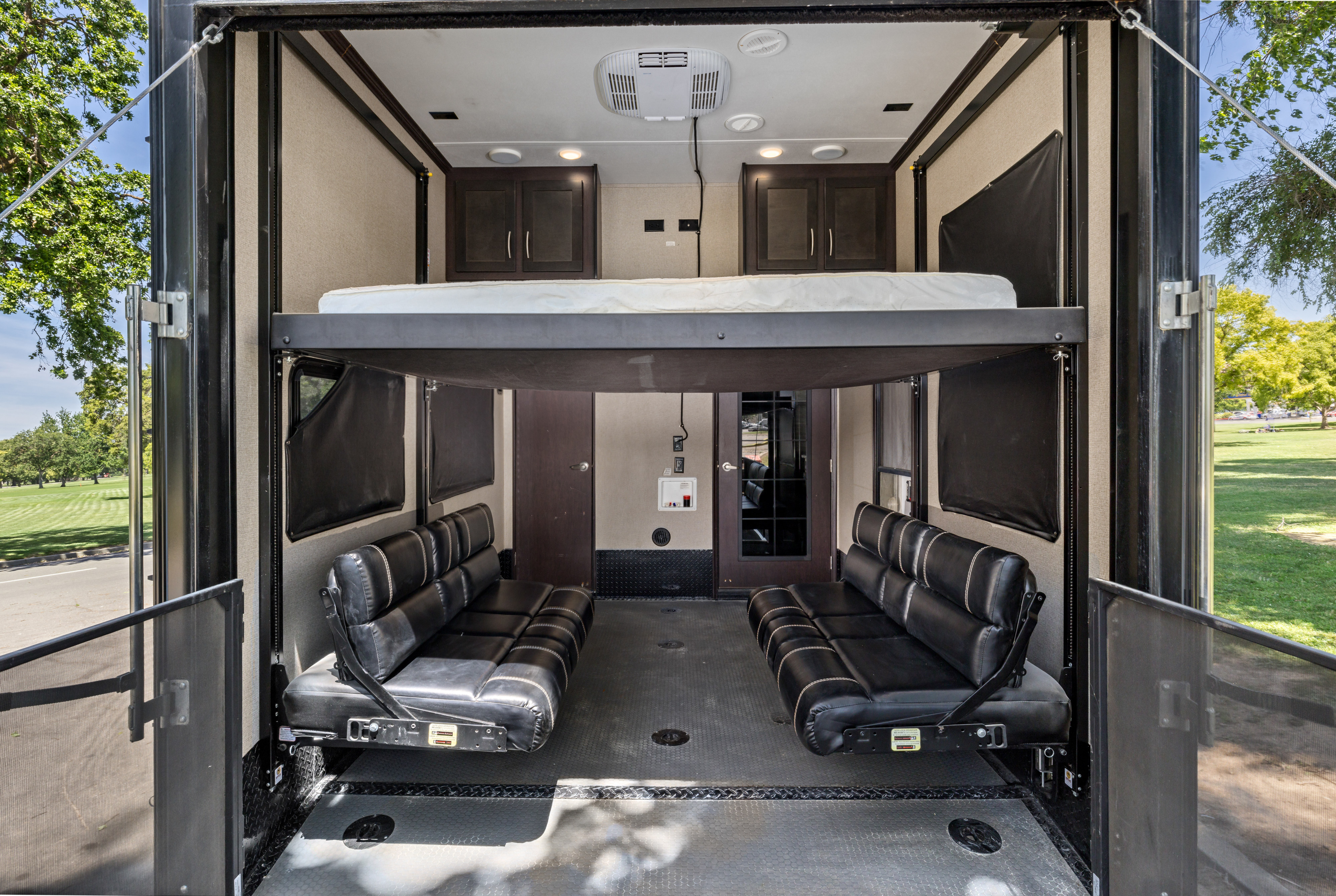 RV rental toy hauler interior with adjustable bed and sofas. Rear ramp open to nature and a grassy field.. Keystone RV Carbon Toy Hauler 2018