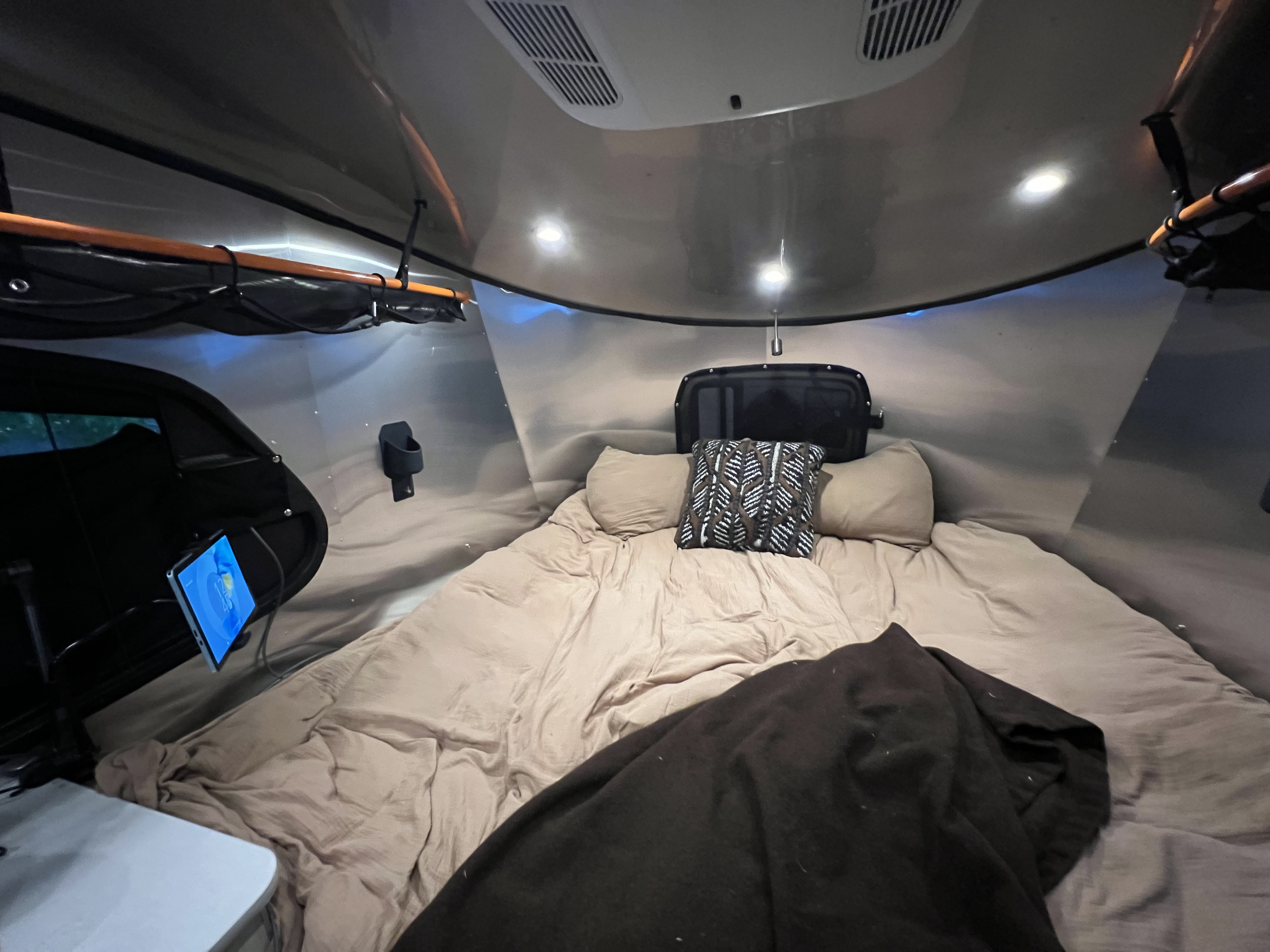 Inside an RV rental: a cozy bed, tablet, and overhead storage, creating a comfortable camper sleeping area.. Airstream Basecamp 2023