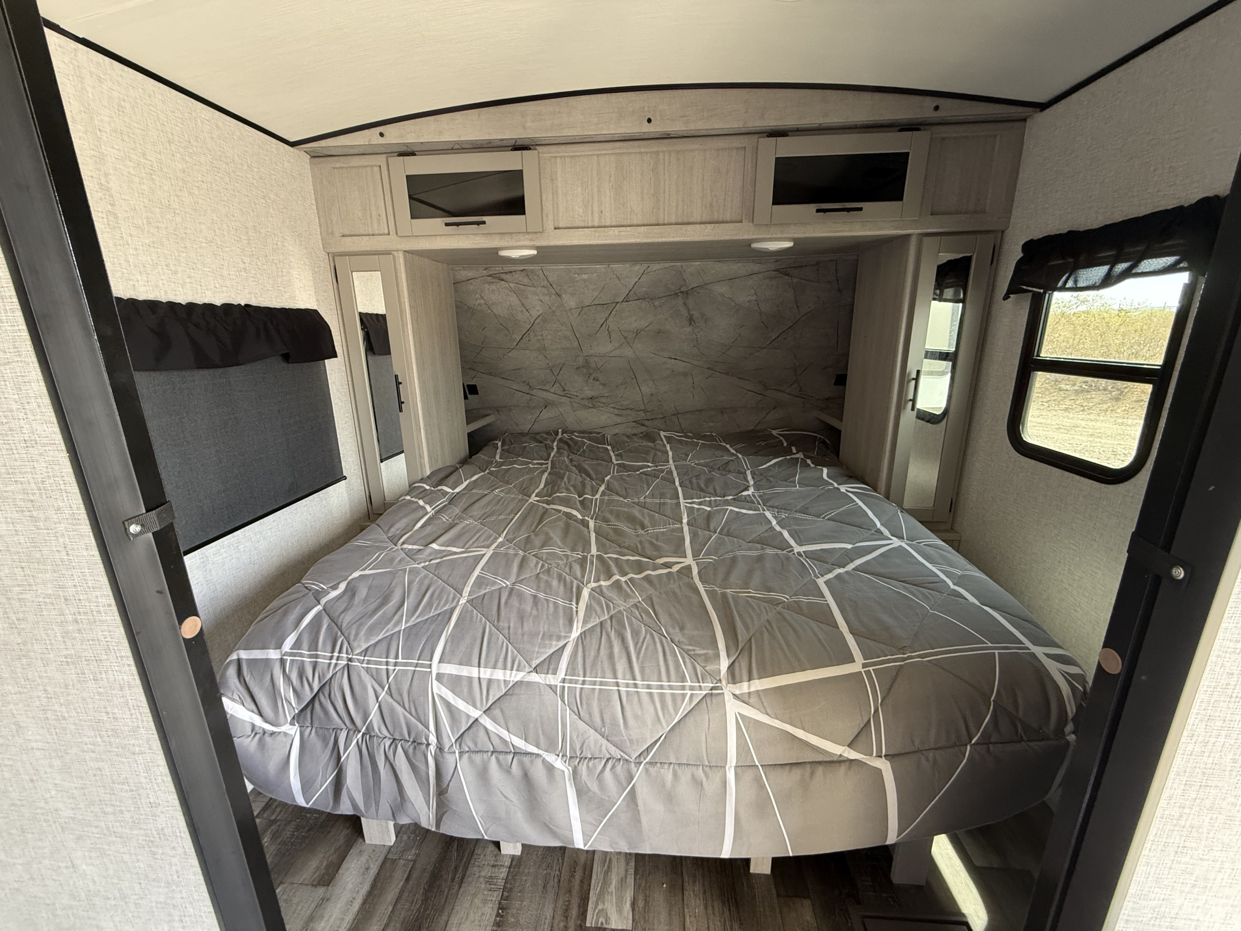 This RV rental bedroom features a comfortable gray bed, overhead cabinets, and mirrored closets, ideal for travel trailer adventures.. Crossroads RV 272BH 2024