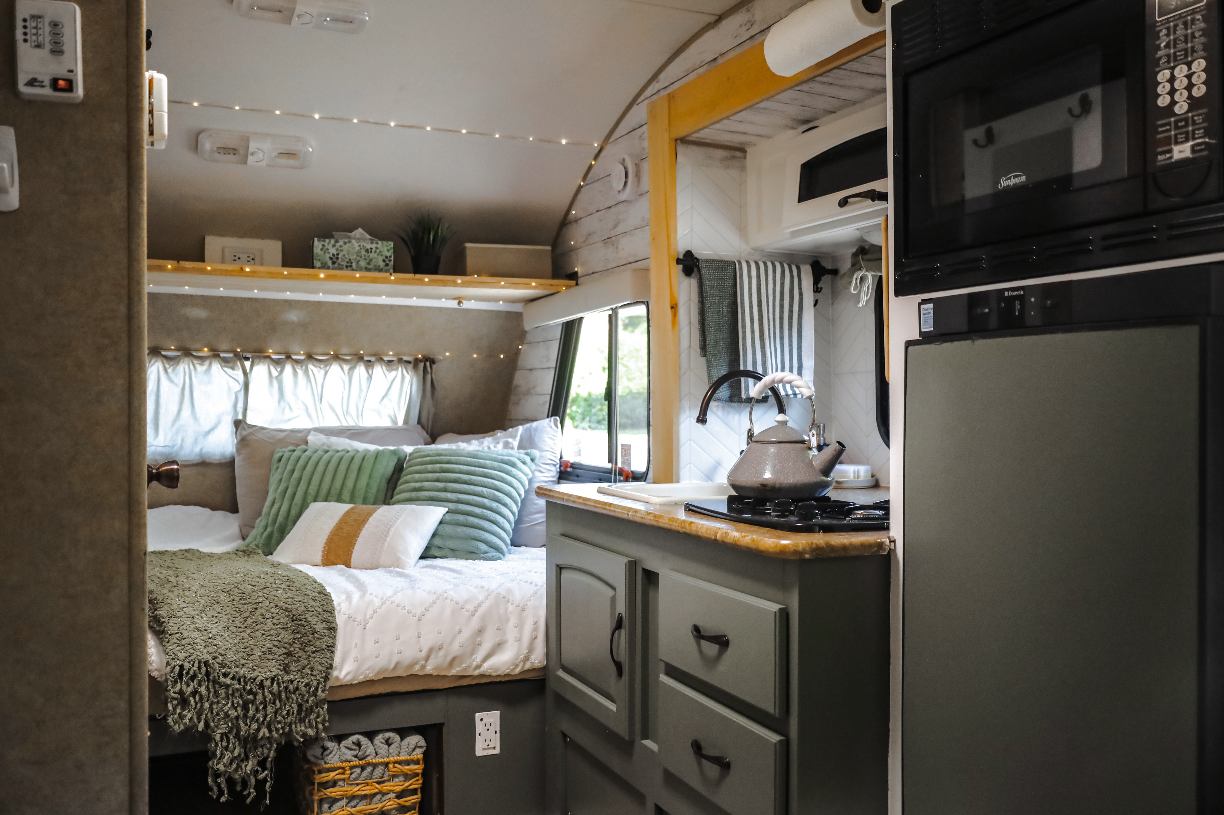 Cozy RV rental interior, showcasing a comfortable bed with string lights and a functional mini-kitchen area.. R-Pod R-Pod Trailer 2012