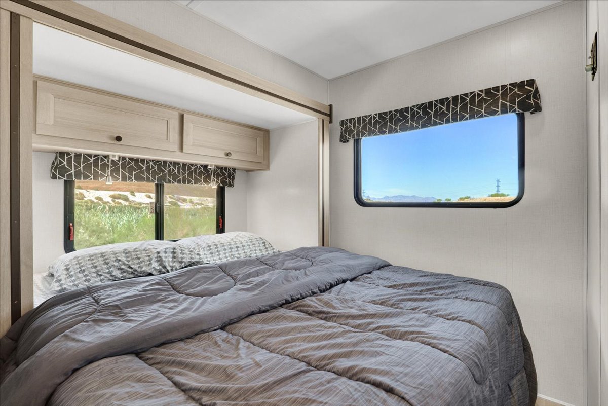 Spacious RV rental bedroom with comfortable bed, overhead cabinets, and large windows offering scenic views.. Forest River Sunseeker 2550 DSLE 2025