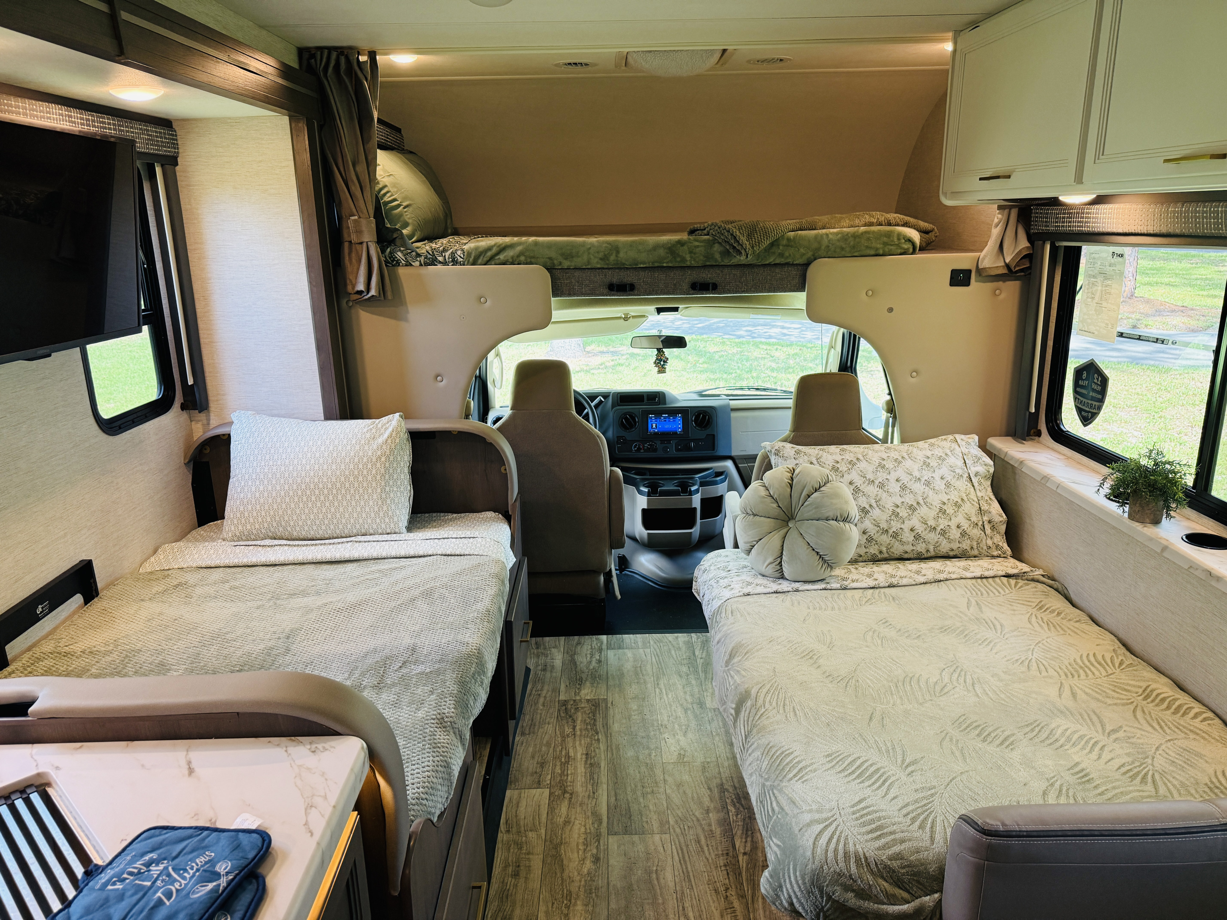 View of an RV rental's inviting interior with two single beds, an overhead bunk, and front cabin.. Thor Chateau 2024