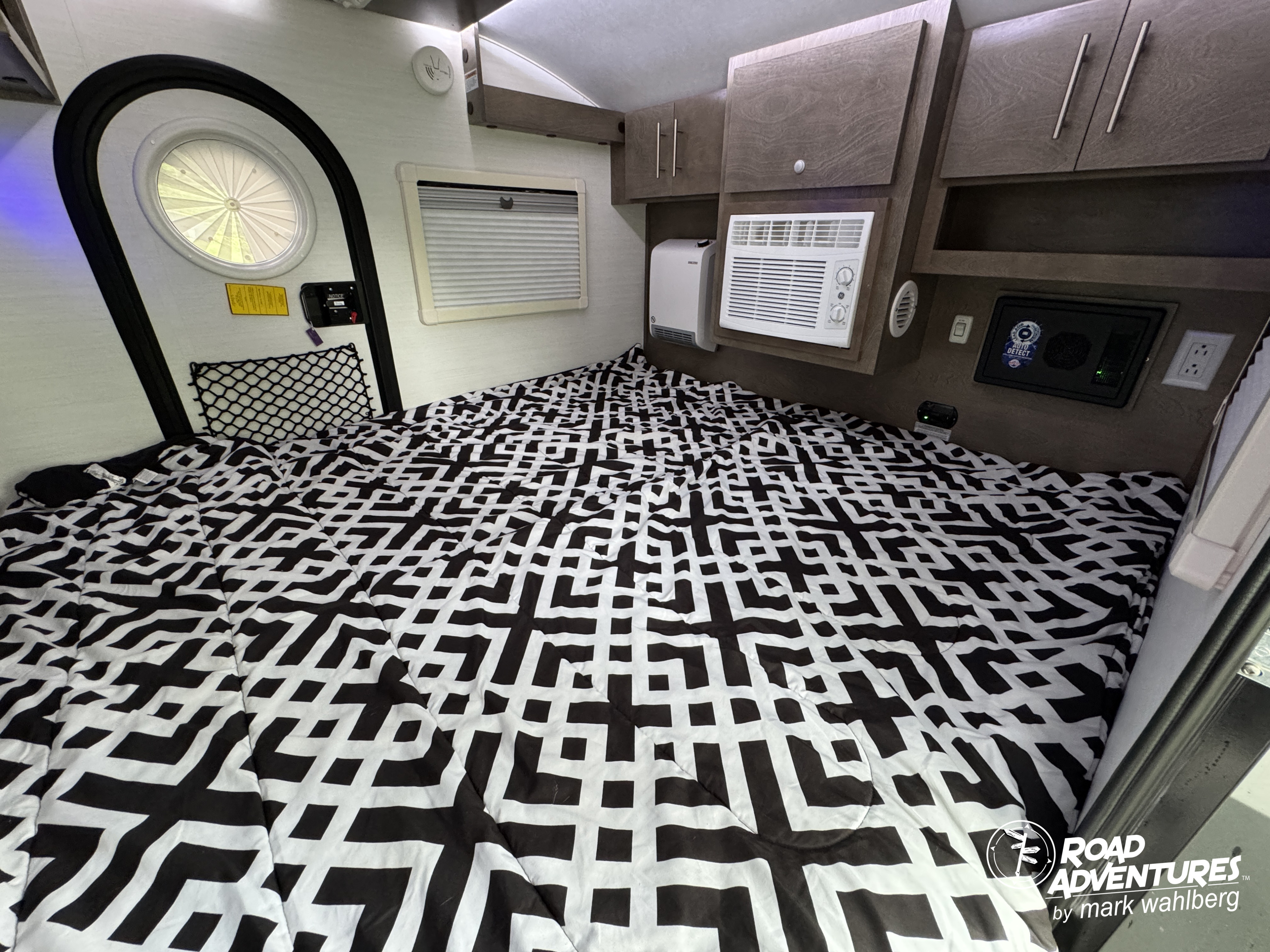 Compact RV rental interior: A bed with geometric comforter, AC, and storage cabinets for comfortable travel.. nuCamp T@G XL 2025