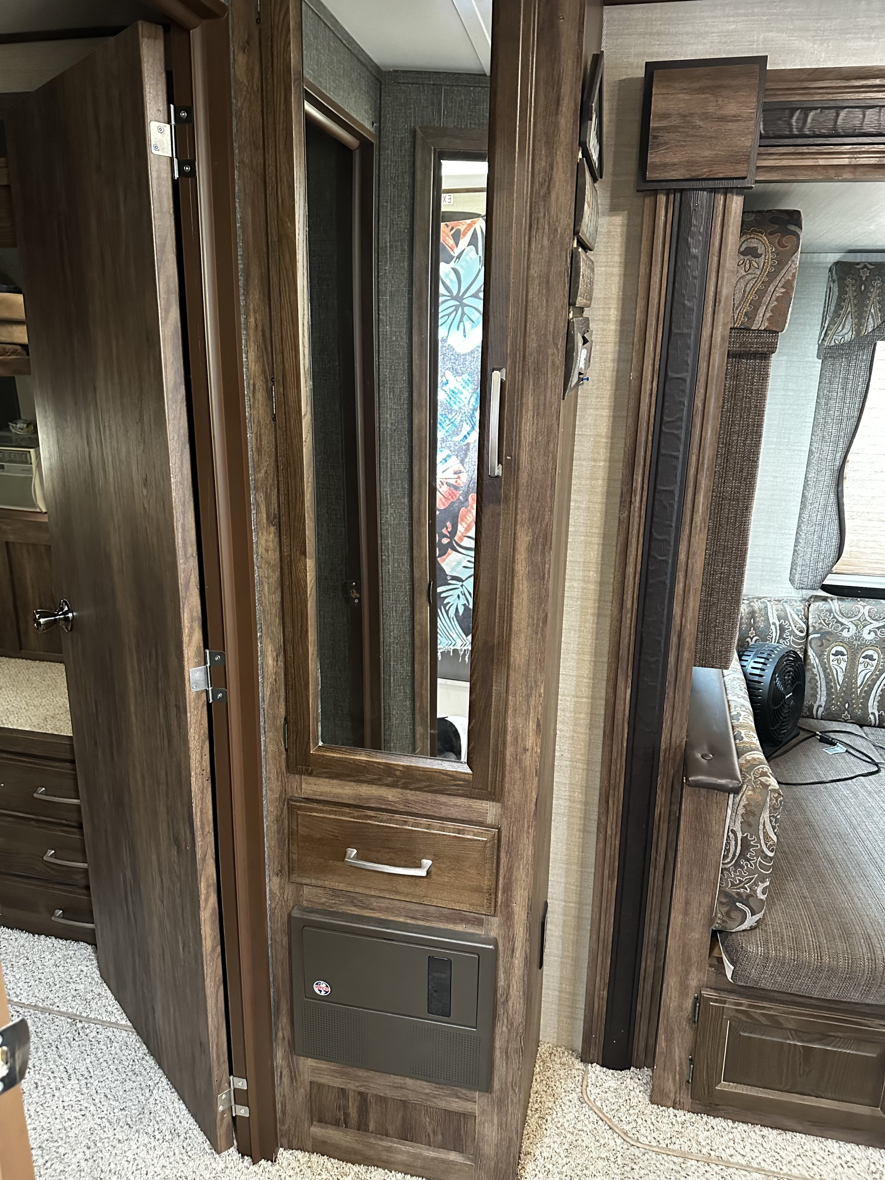 RV rental interior showcasing dark wood cabinetry, a mirrored panel, and a cozy seating area with a fan and electrical panel.. Keystone RV Cougar 2016