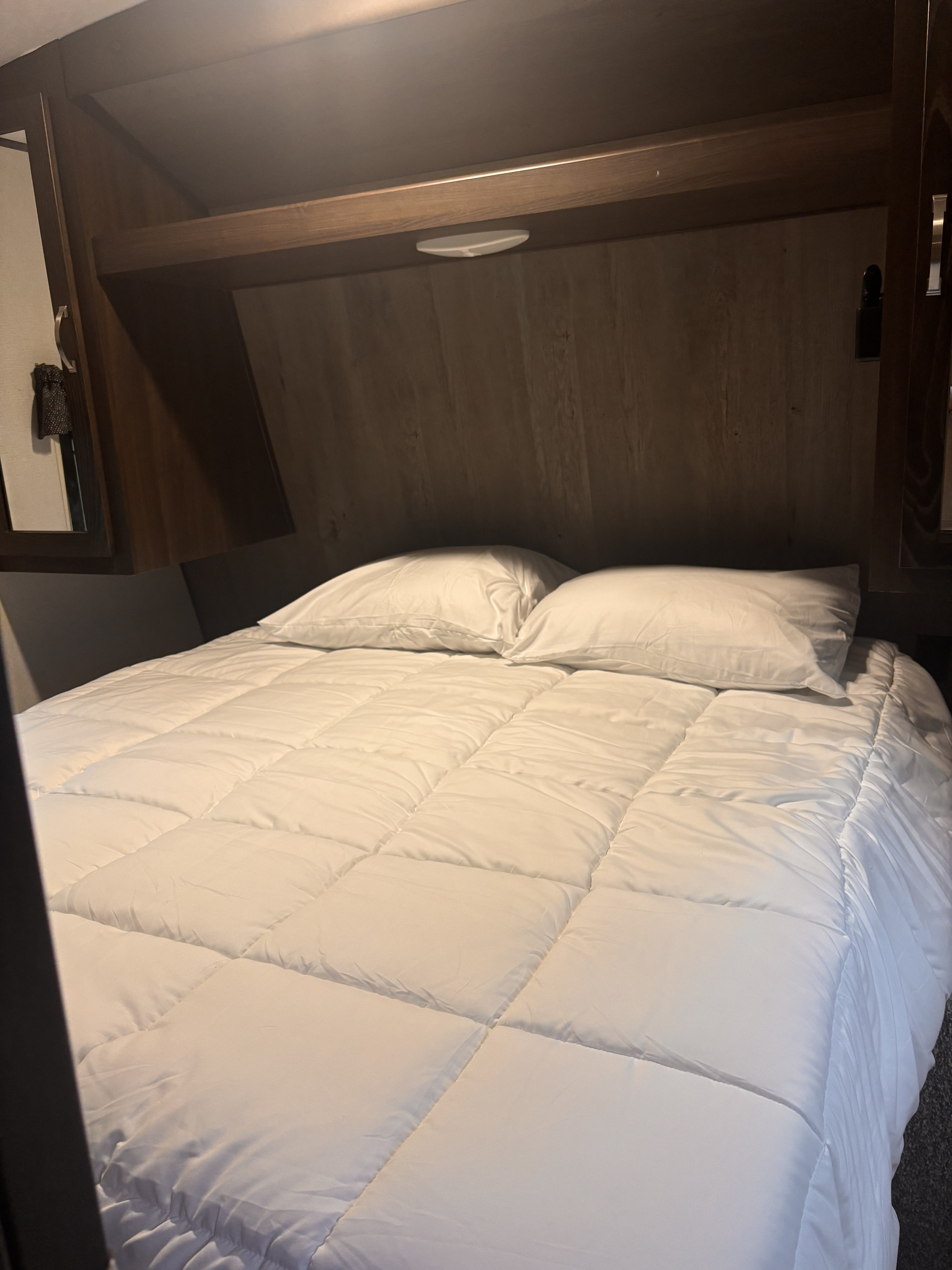 Cozy RV rental bedroom with a comfy white bed, pillows, and overhead storage.. Keystone RV Springdale 2020