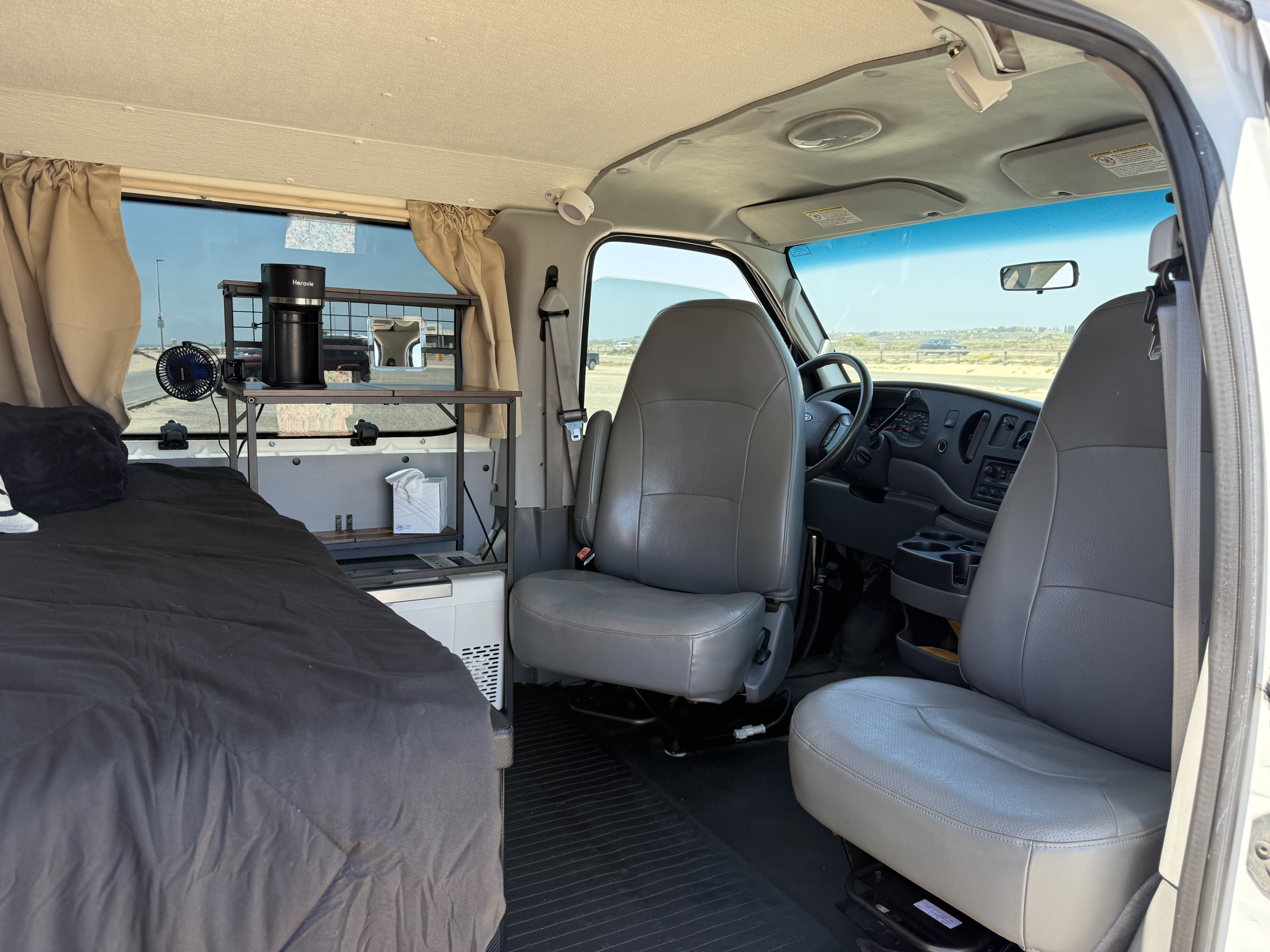 Spacious rv rental interior featuring a cozy bed, mini kitchen setup, and comfortable front seats for your next adventure.. Ford Econoline 150 2007