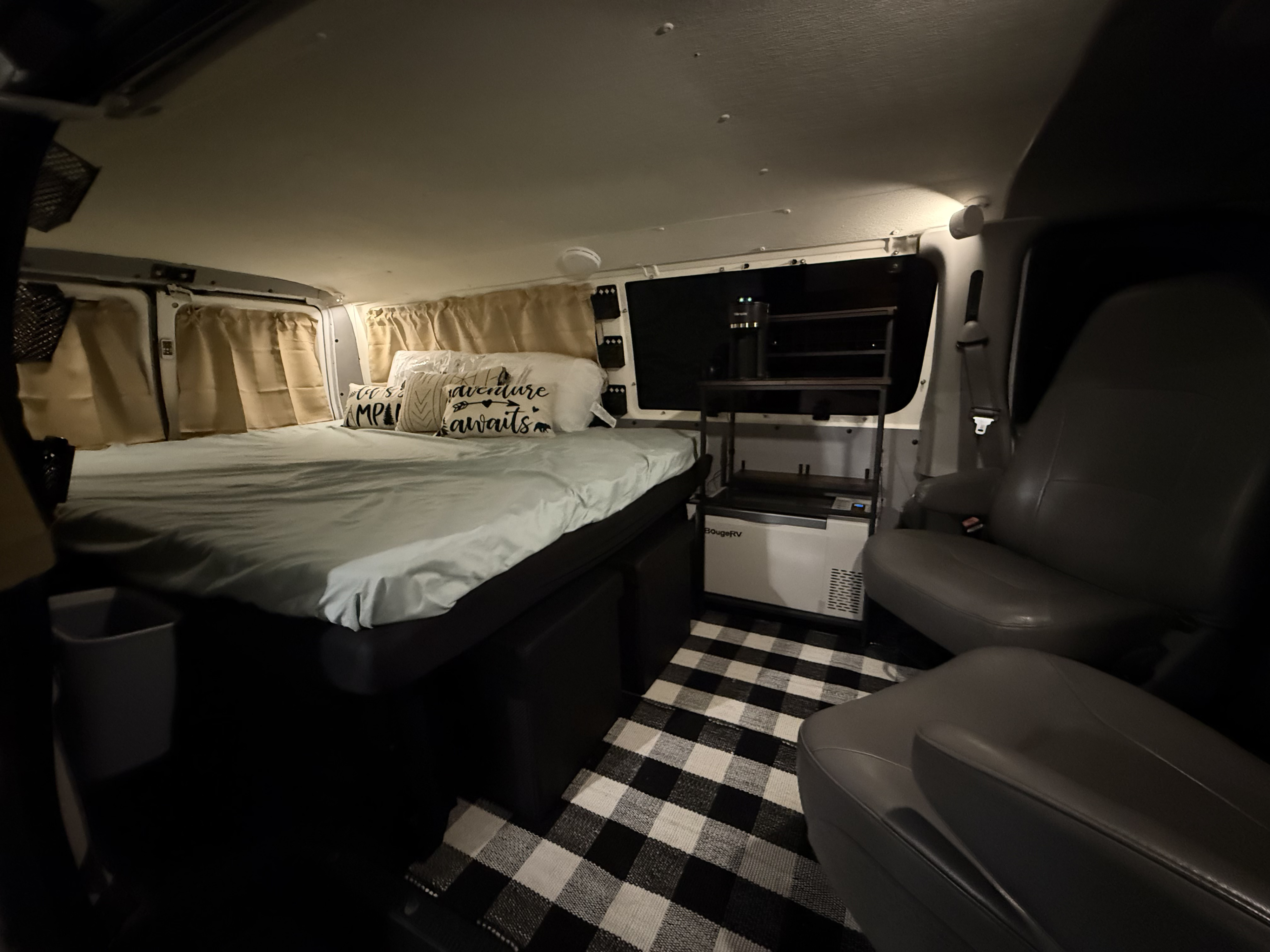 This cozy RV rental interior features a full bed, built-in fridge with shelves, and a black and white checkered rug for comfy camper living.. Ford Econoline 150 2007