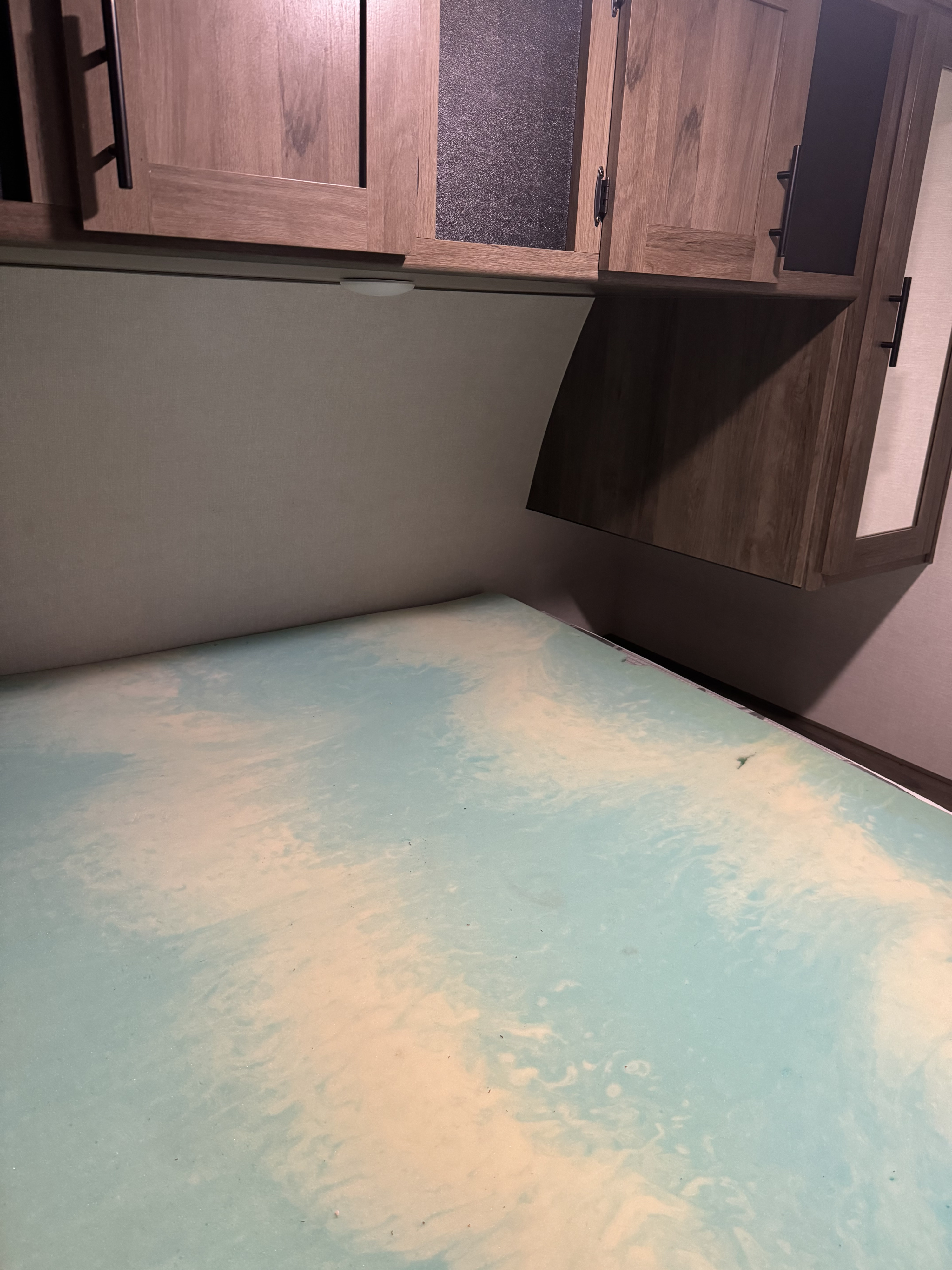RV rental interior: A bed with a swirled blue and cream foam topper is positioned under wood cabinets.. Avenger Avenger Trailer 2021
