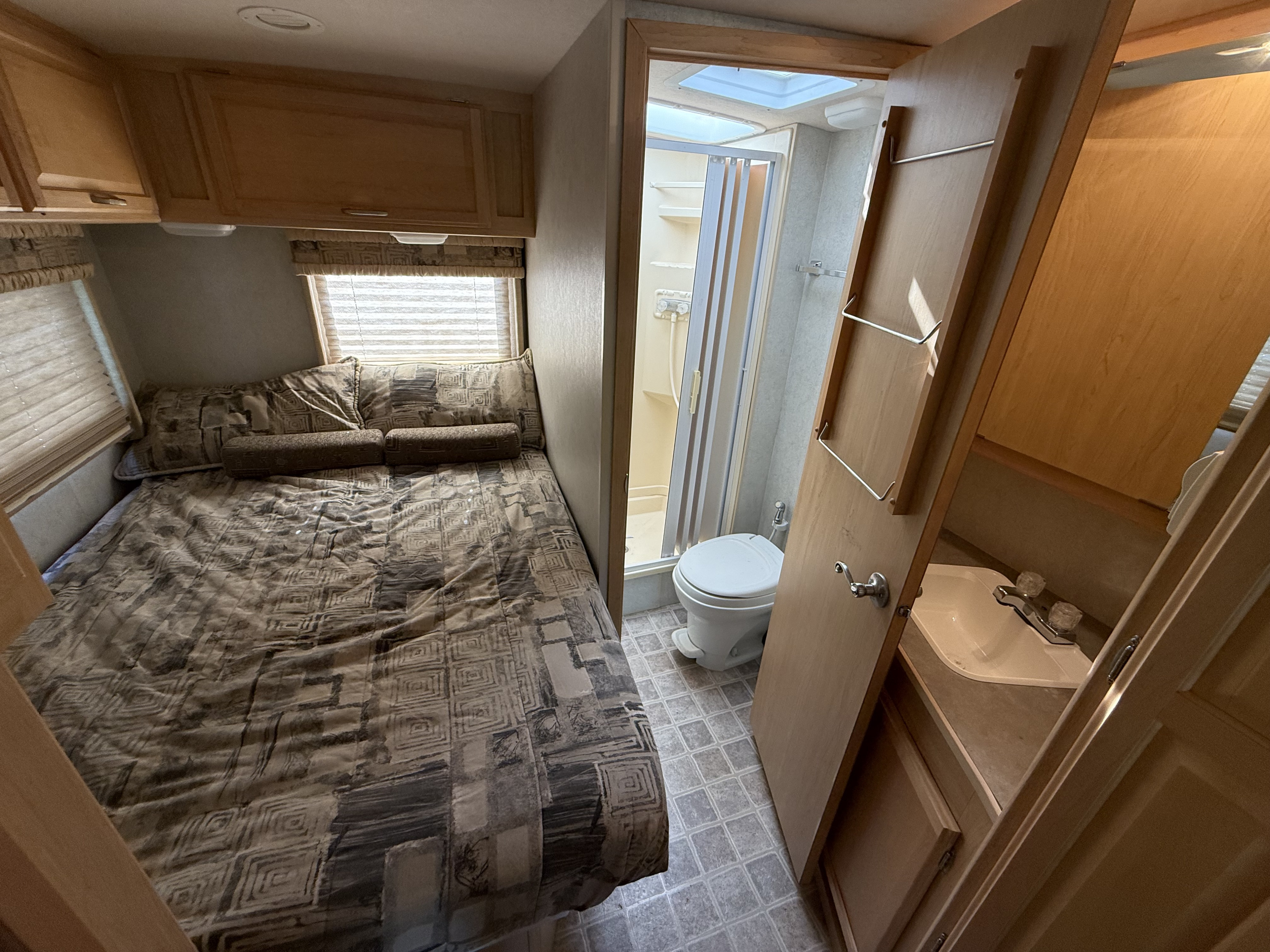 RV rental interior: bedroom with patterned bed, windows, overhead cabinets; adjoining compact bathroom has shower, toilet, and sink.. Winnebago Aspect 2005