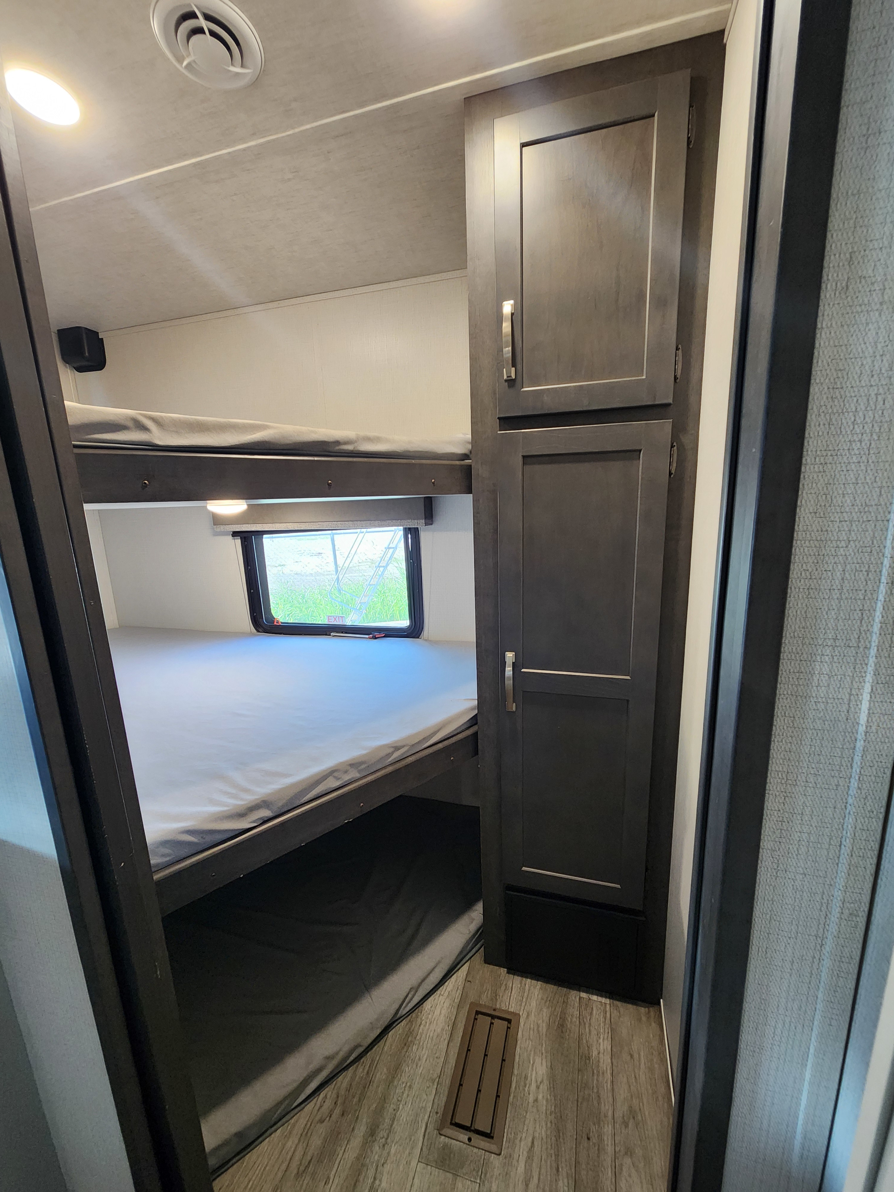 RV rental interior features cozy dark wood bunk beds, ample storage in built-in cabinet, and a window.. Keystone RV Cougar 2024