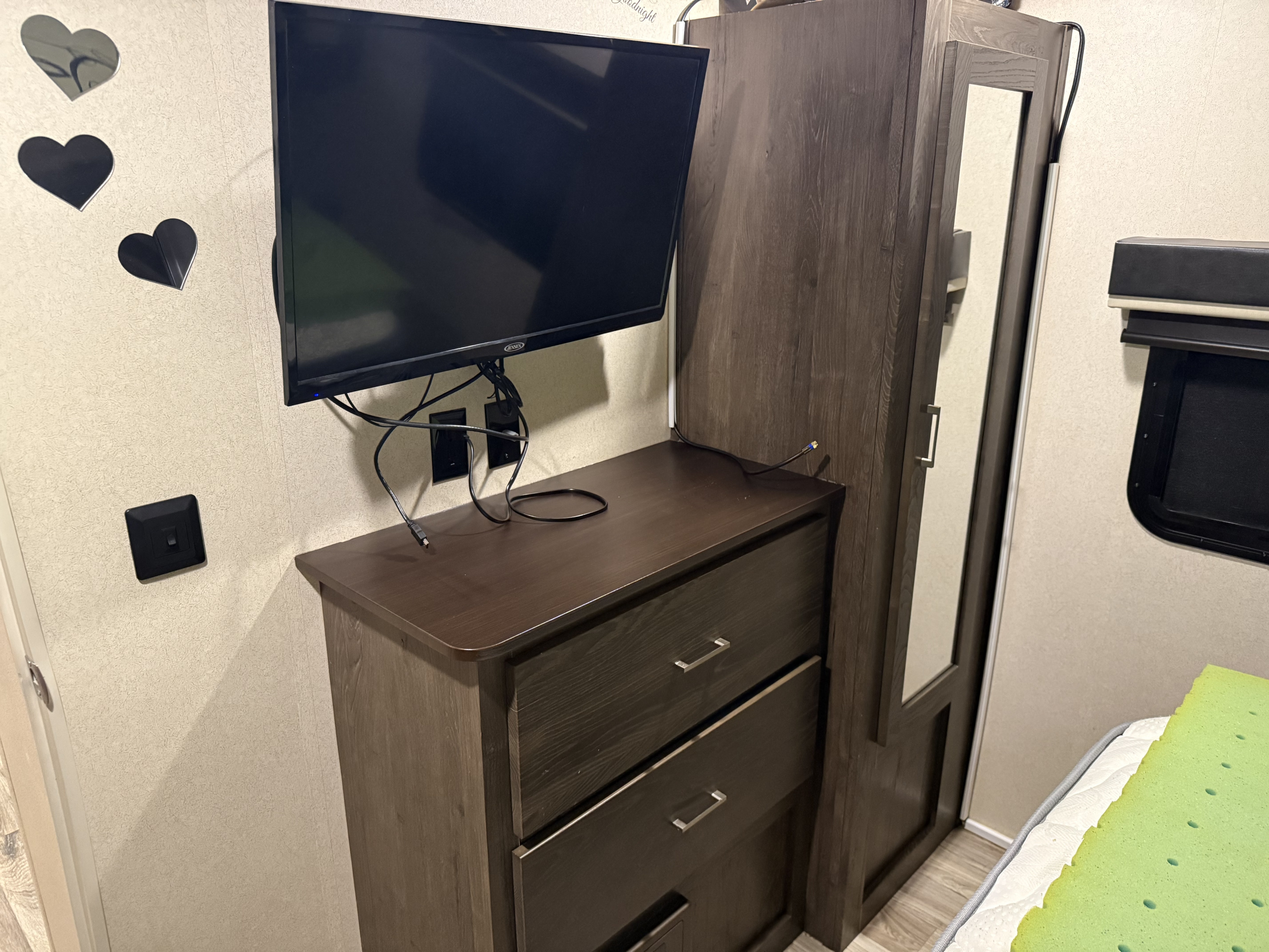 Interior of an RV rental, featuring a mounted TV above a dark wood dresser, alongside a mirrored wardrobe. Wall decor includes hearts.. Forest River Salem Hemisphere Lite 2018
