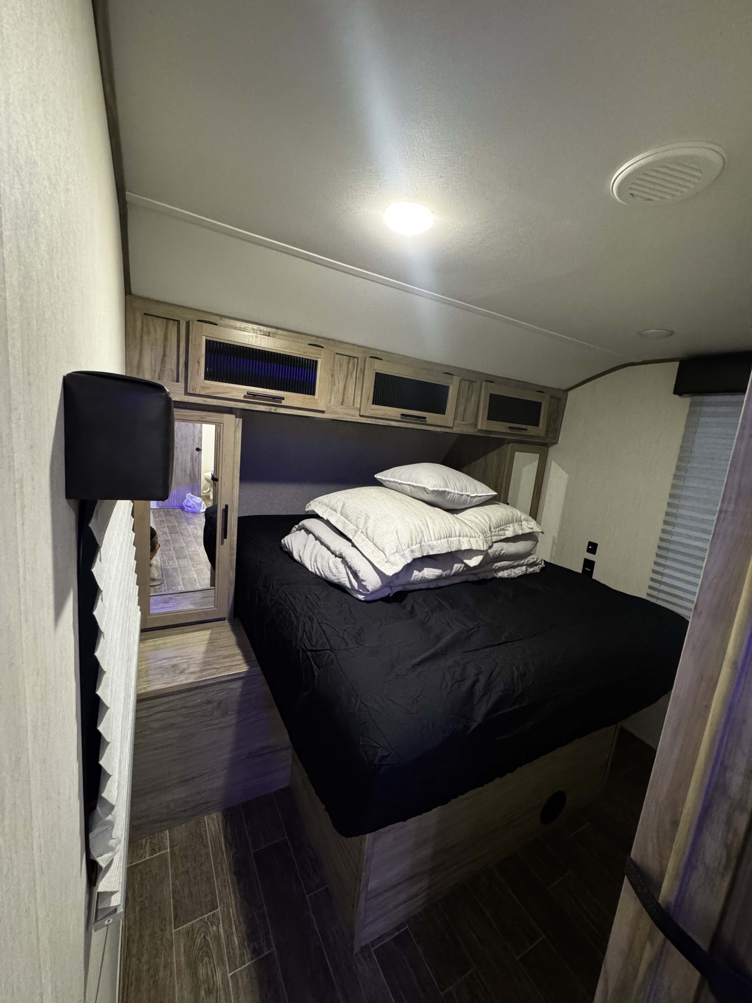Bright RV rental bedroom interior with queen bed, overhead cabinets, and pleated blinds, offering compact comfort.. Forest River Cherokee Alpha Wolf 2022