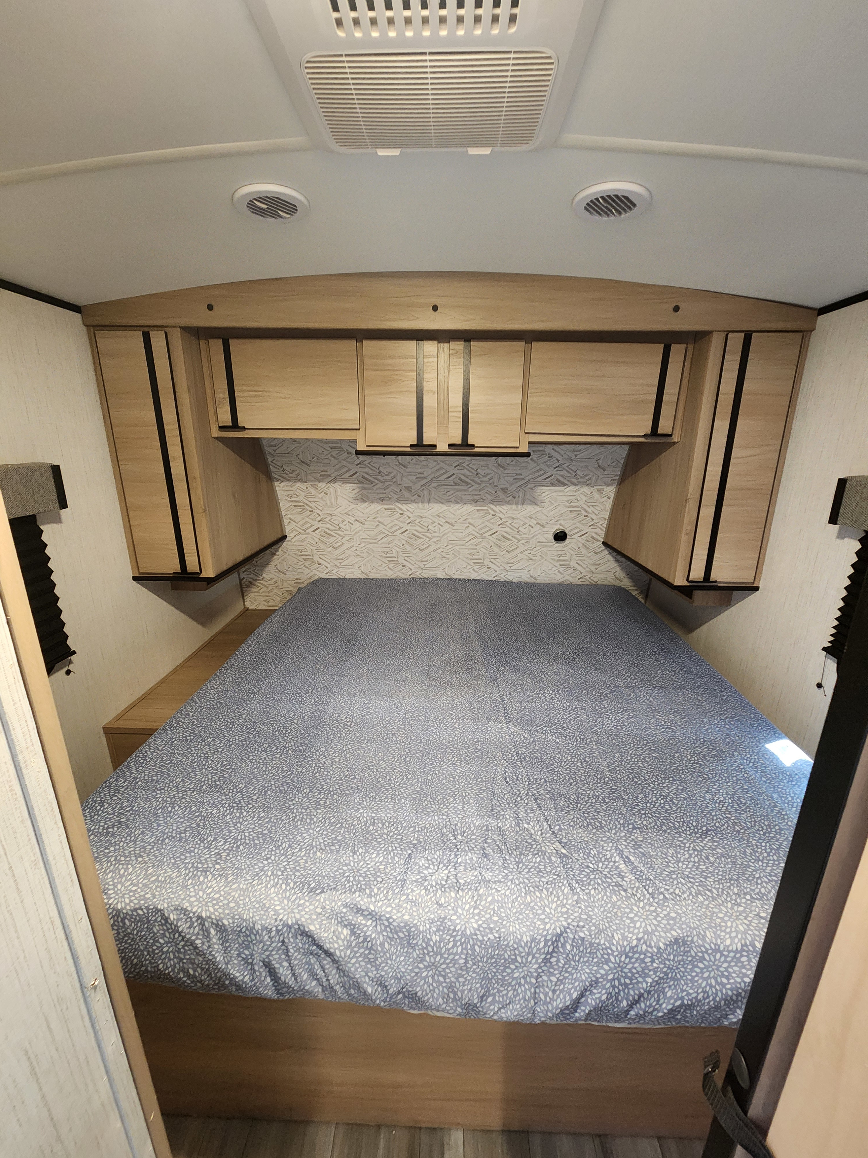 Cozy RV rental bedroom featuring a patterned bedspread, overhead storage, and ceiling vents.. Cruiser RV Radiance 2022