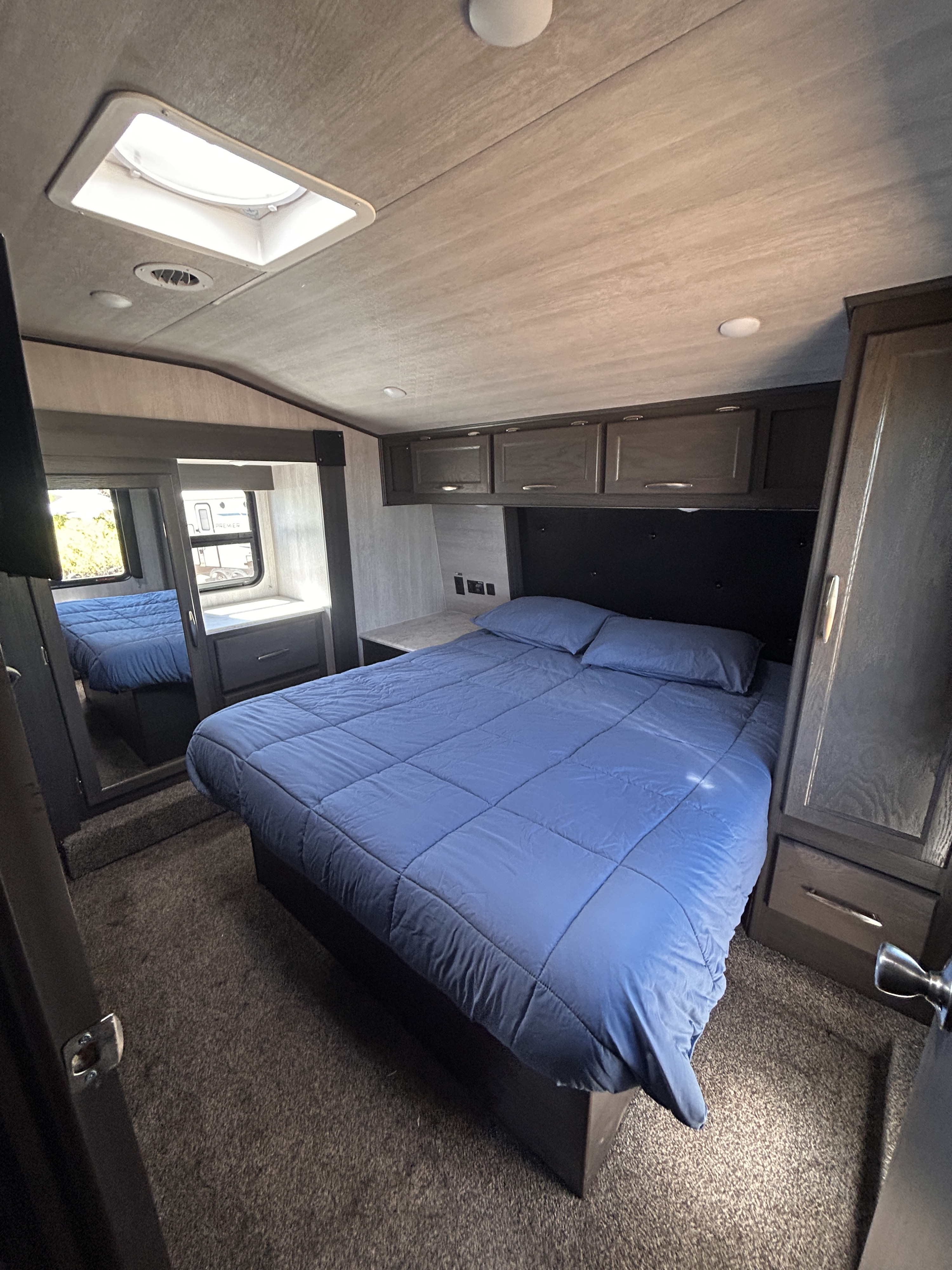 Spacious RV rental bedroom with a comfy blue bed, overhead cabinets, and a bright ceiling skylight.. genesis 28CRT 2022