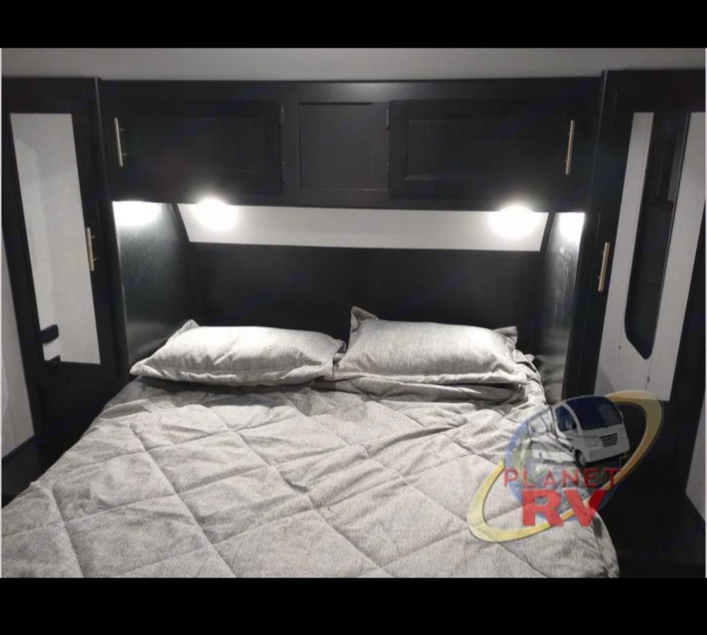 Cozy RV rental bedroom with gray bedding, overhead cabinets, and reading lights, ready for a comfortable night's sleep.. Forest River Cherokee 2022