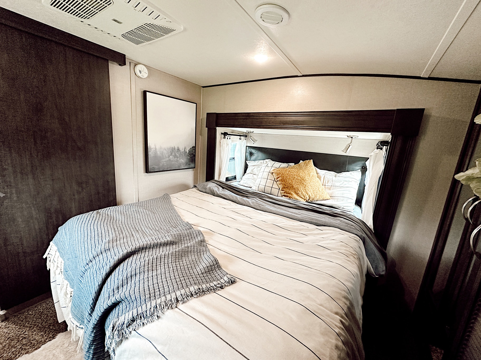 Enjoy a cozy RV rental bedroom. Features a comfy bed with striped bedding, throw blanket, wall art, and AC vents.. Forest River Shasta Phoenix 2020