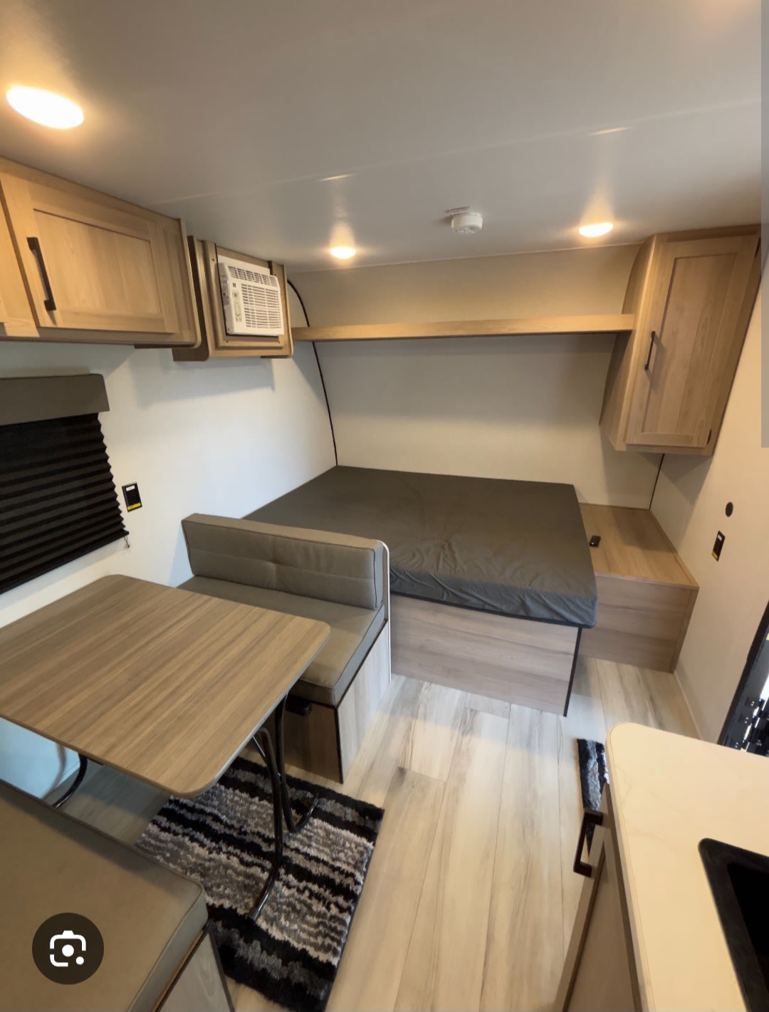 RV rental interior shows a cozy bed, dining area with table & benches, storage cabinets, and a partial kitchen counter.. Coleman 17b 2025