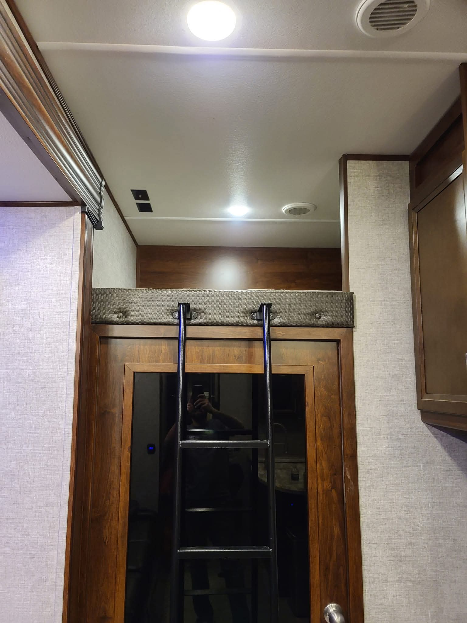 RV rental interior: A cozy loft bunk bed with a black metal ladder over a wooden door. Ceiling lights and vents are visible.. Forest River Vengeance 2019