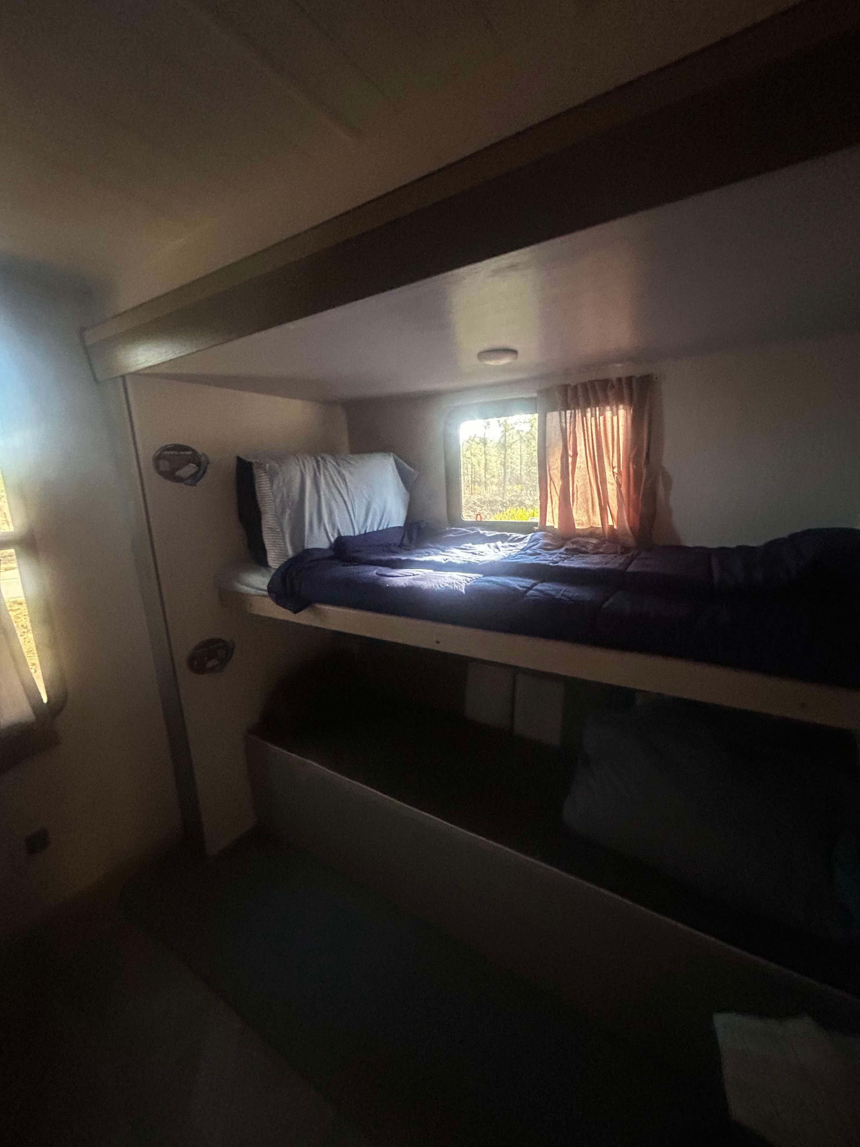 Cozy RV rental interior with sunlight illuminating comfortable bunk beds and a view of trees outside.. Forest River Salem Platinum 2024