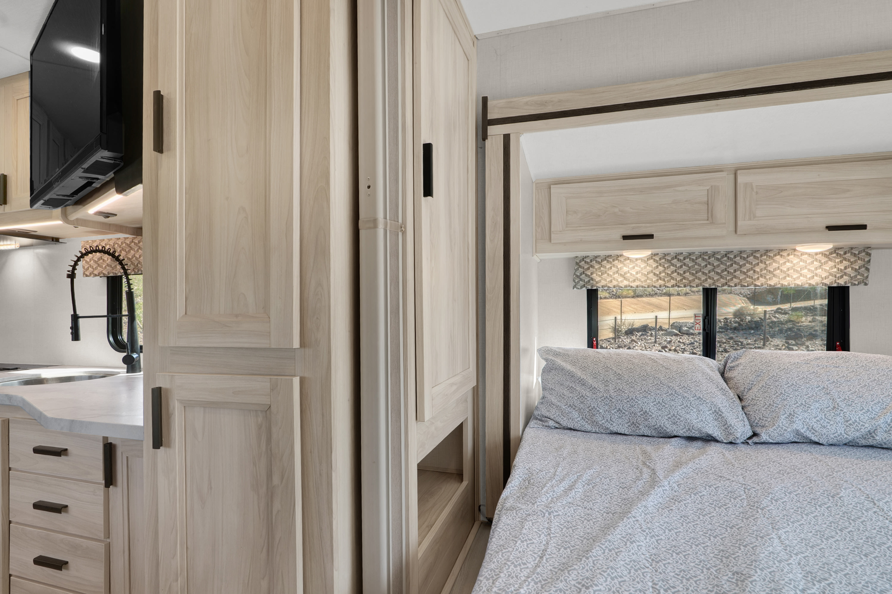 Modern RV rental interior showing a compact kitchen with sink and TV, and a cozy bedroom with patterned bedding.. Forester LE 2023