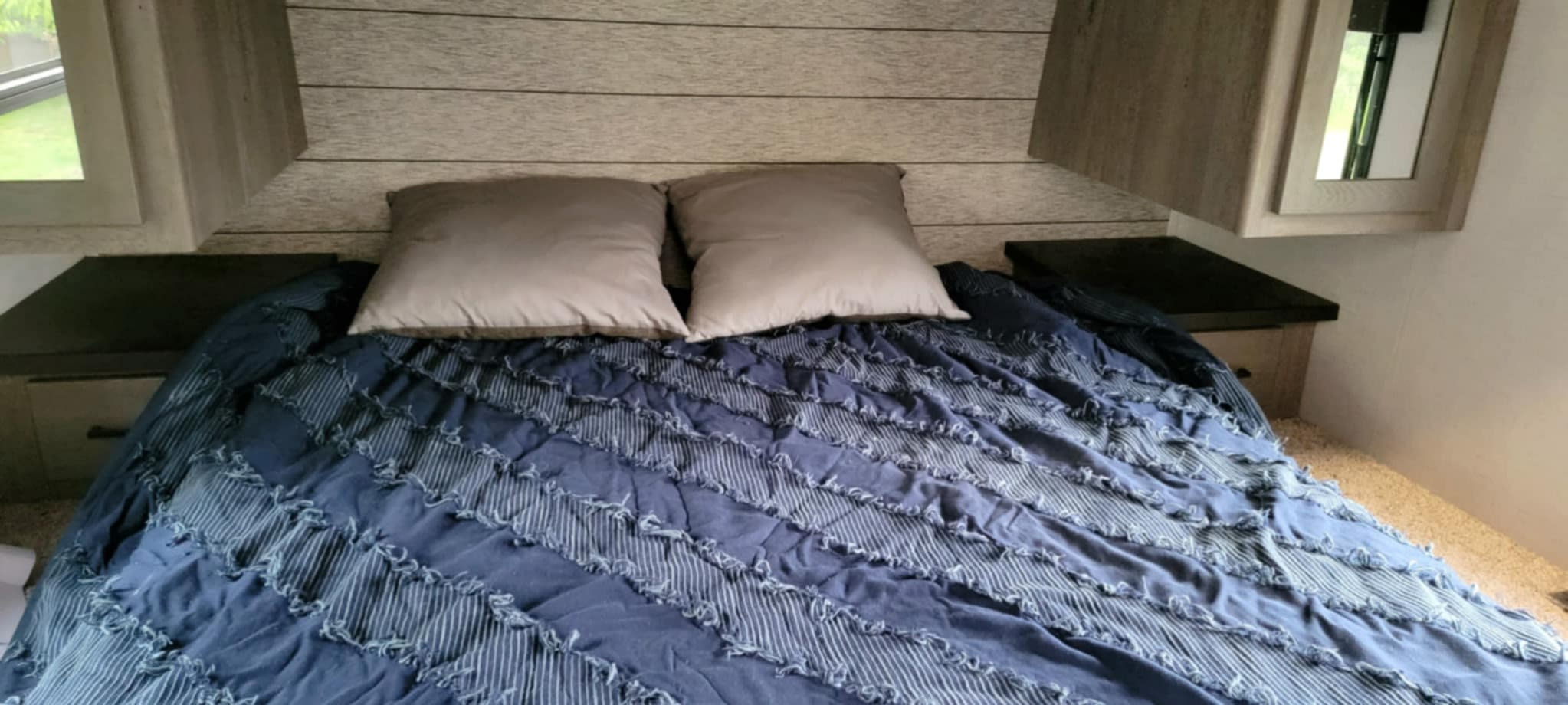 Inside an RV rental: a cozy bedroom with a blue textured comforter, two pillows, and light wood-paneled walls.. Keystone Carbon 2021