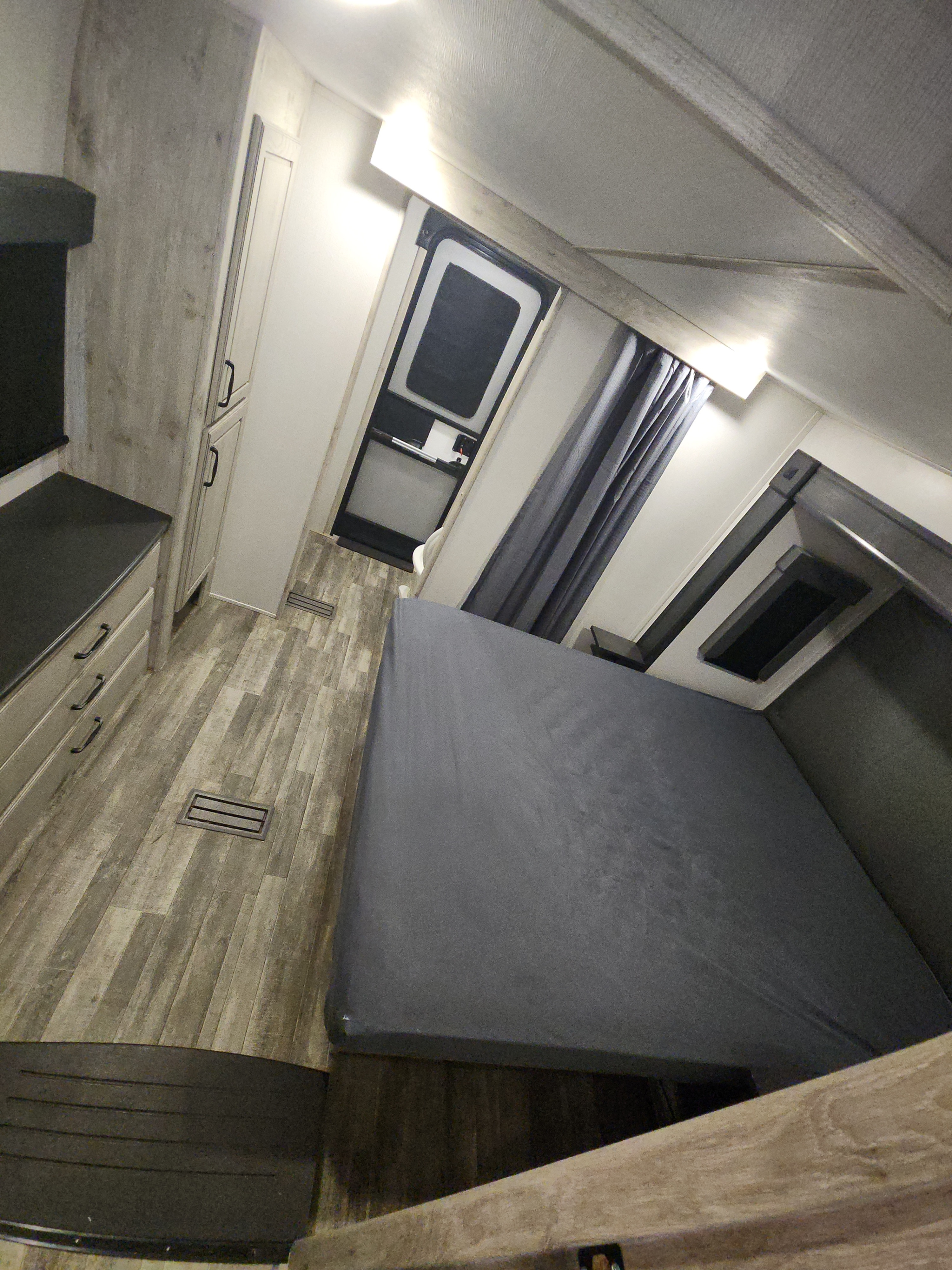 Interior of an RV rental bedroom, featuring a large gray bed, wood-look flooring, built-in dresser, and an exterior door.. Keystone RV Avalanche 2023