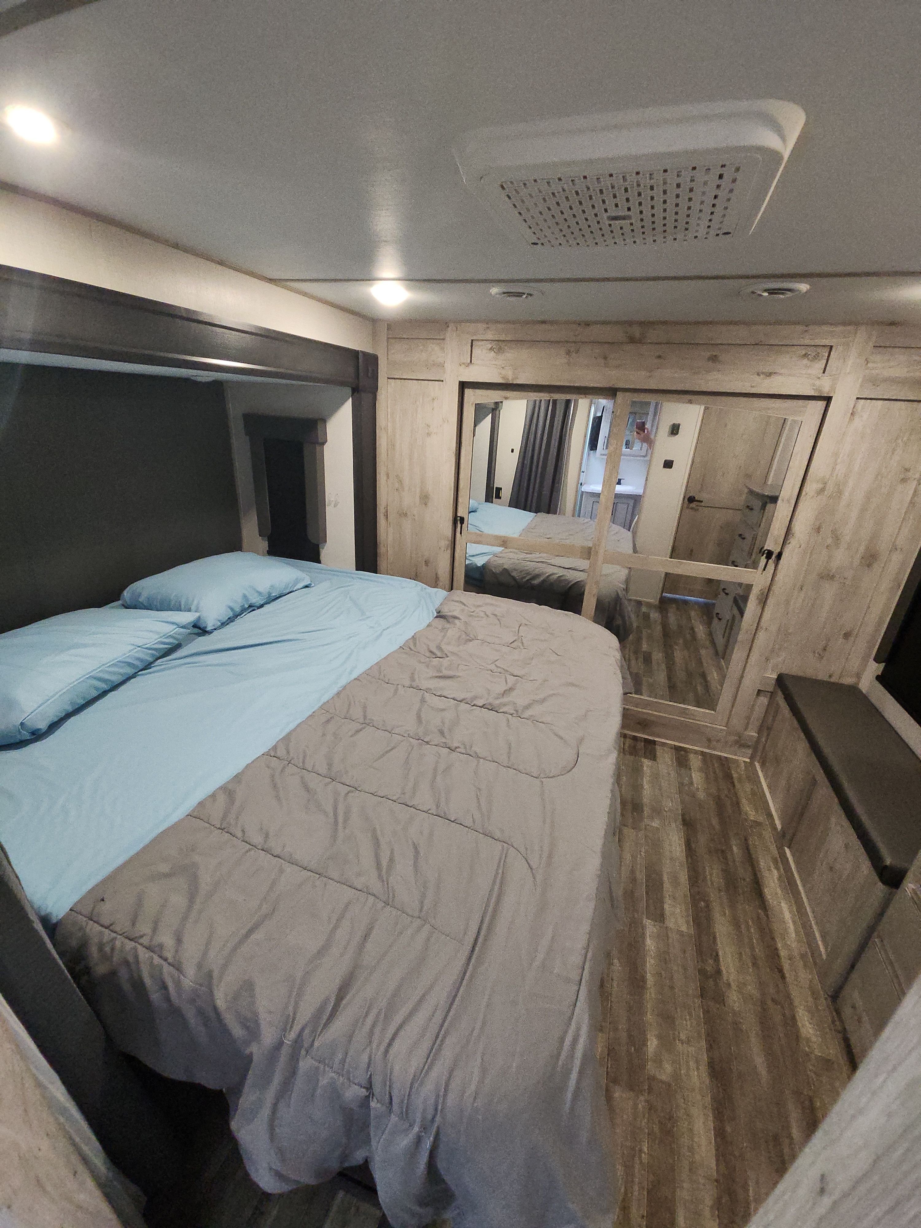 Cozy RV rental bedroom with a comfortable bed, wood flooring, and mirrored closet, offering travel comfort.. Keystone RV Avalanche 2023